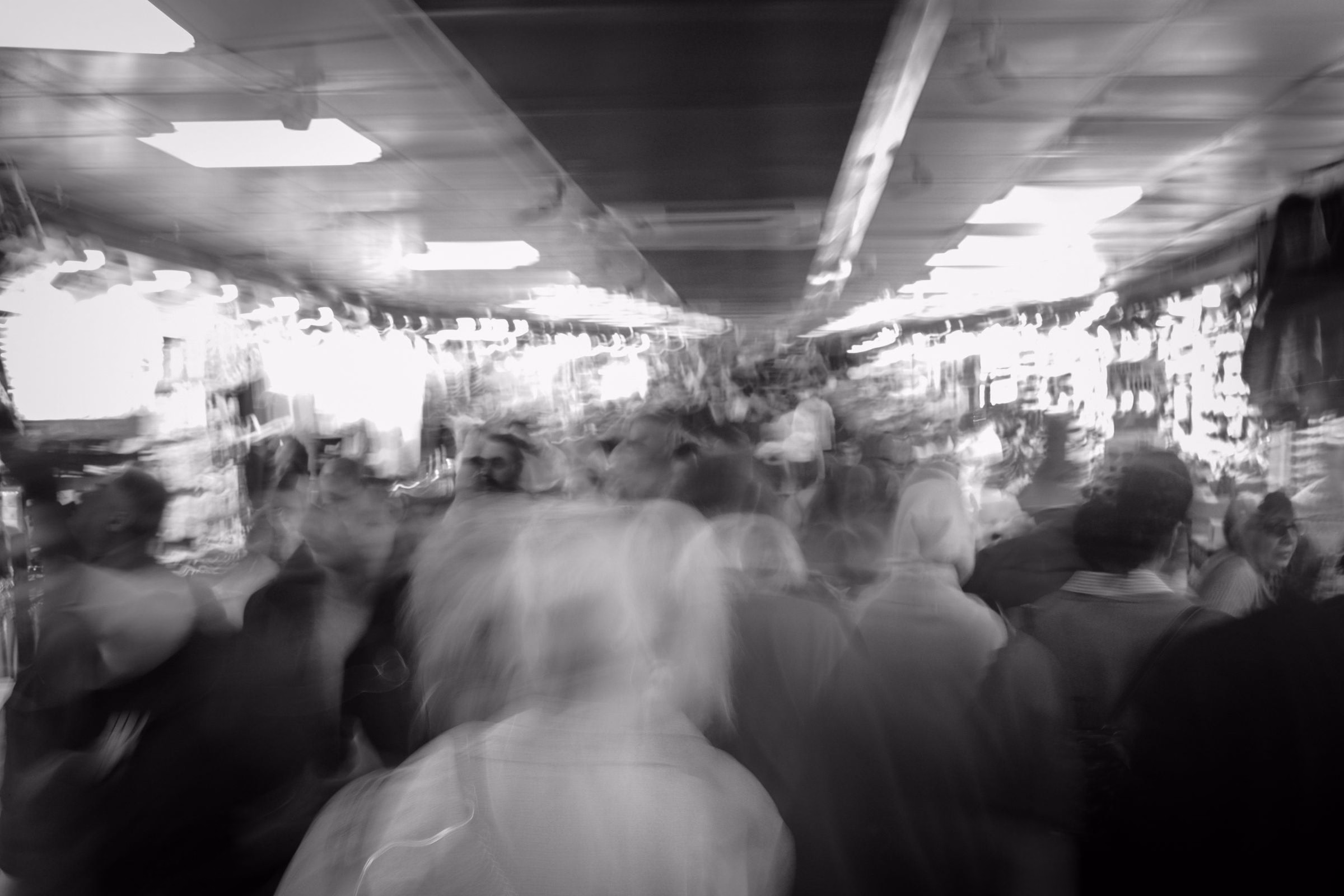 A blurred crowd moving through a busy market hall, in black and white