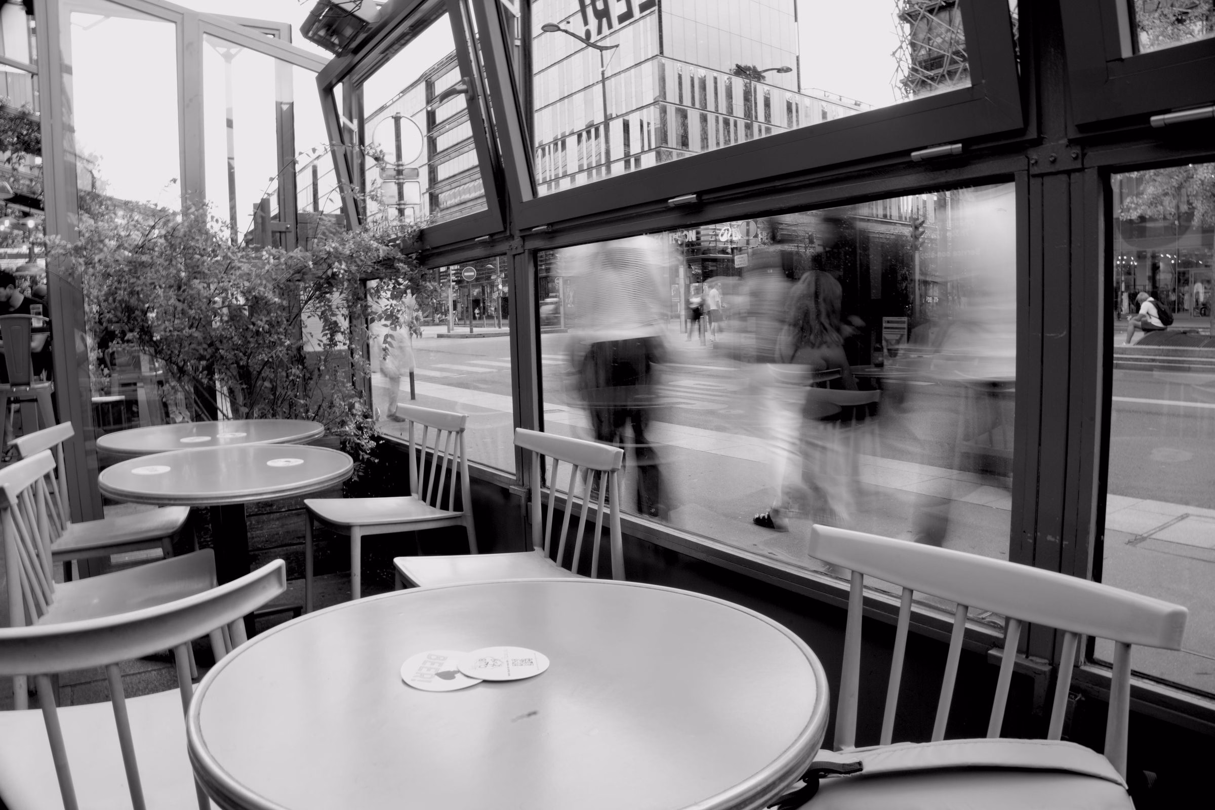 Empty cafe terrace tables with blurred people walking past on the street, in black and white