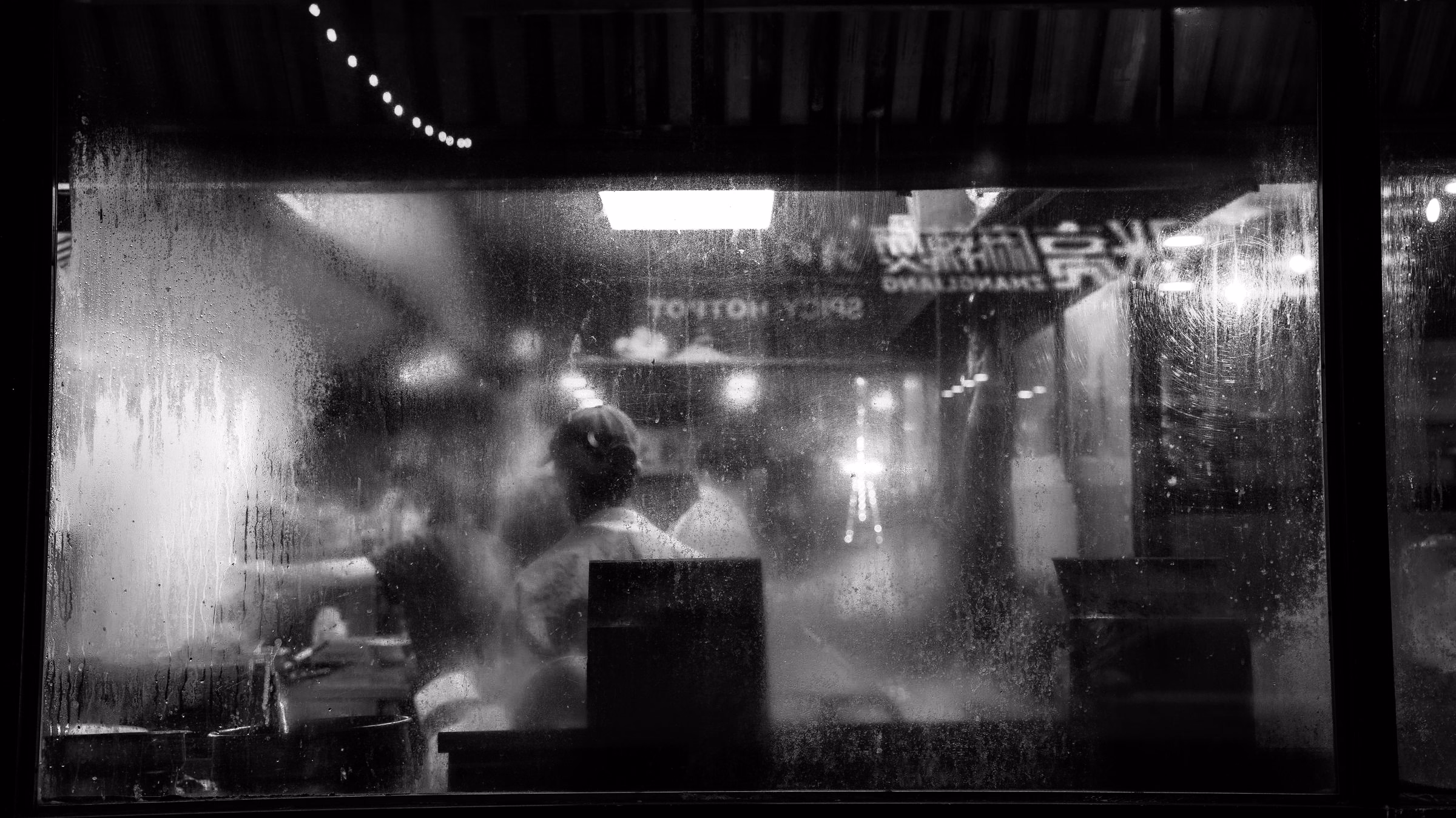 A busy restaurant kitchen seen through a steamed-up window at night, in black and white