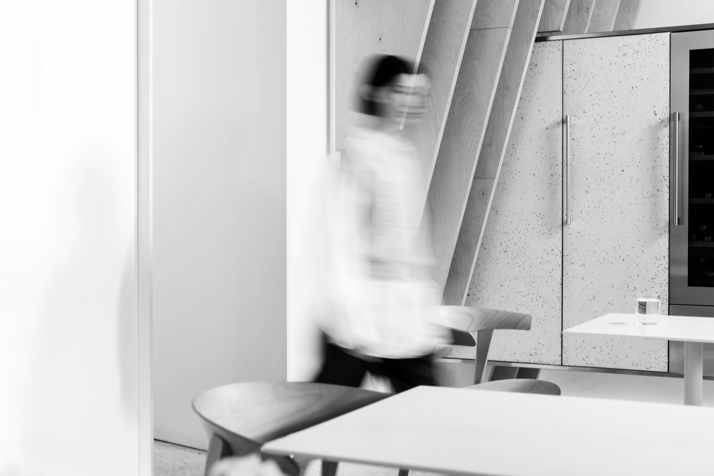 A blurred figure walking between tables in a bright cafe, in black and white