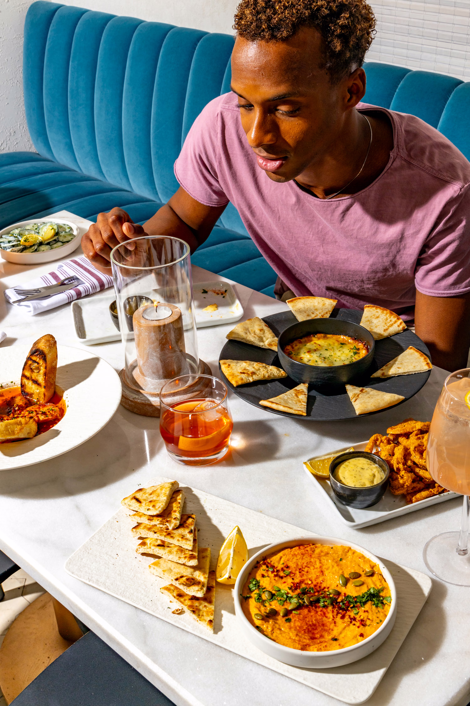 A guest reaching for shared plates of dips, flatbread and cocktails at Mistora