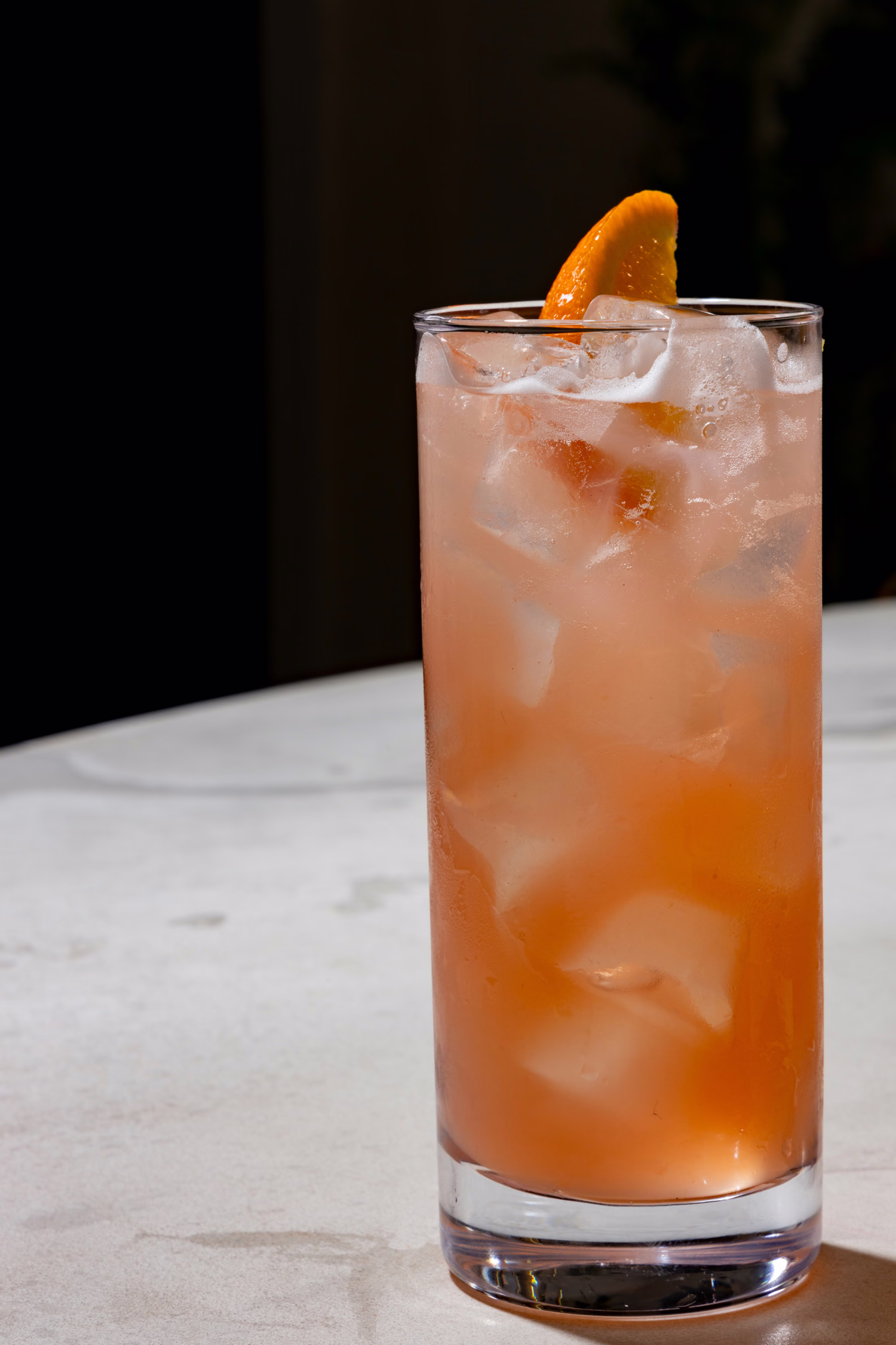 A tall pink highball with an orange wedge at Mistora
