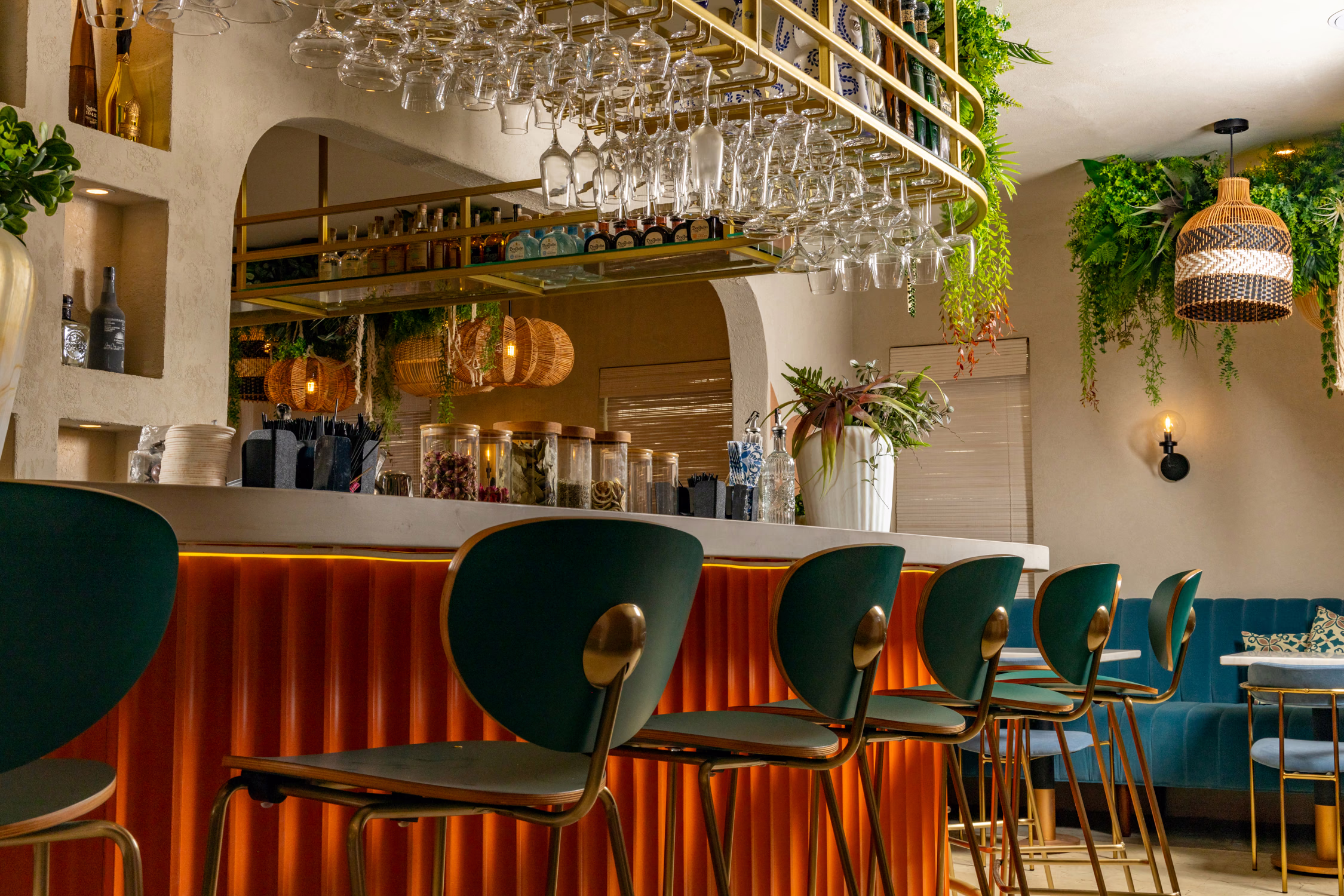 The bar at Mistora, with green stools, an orange fluted front and hanging glassware
