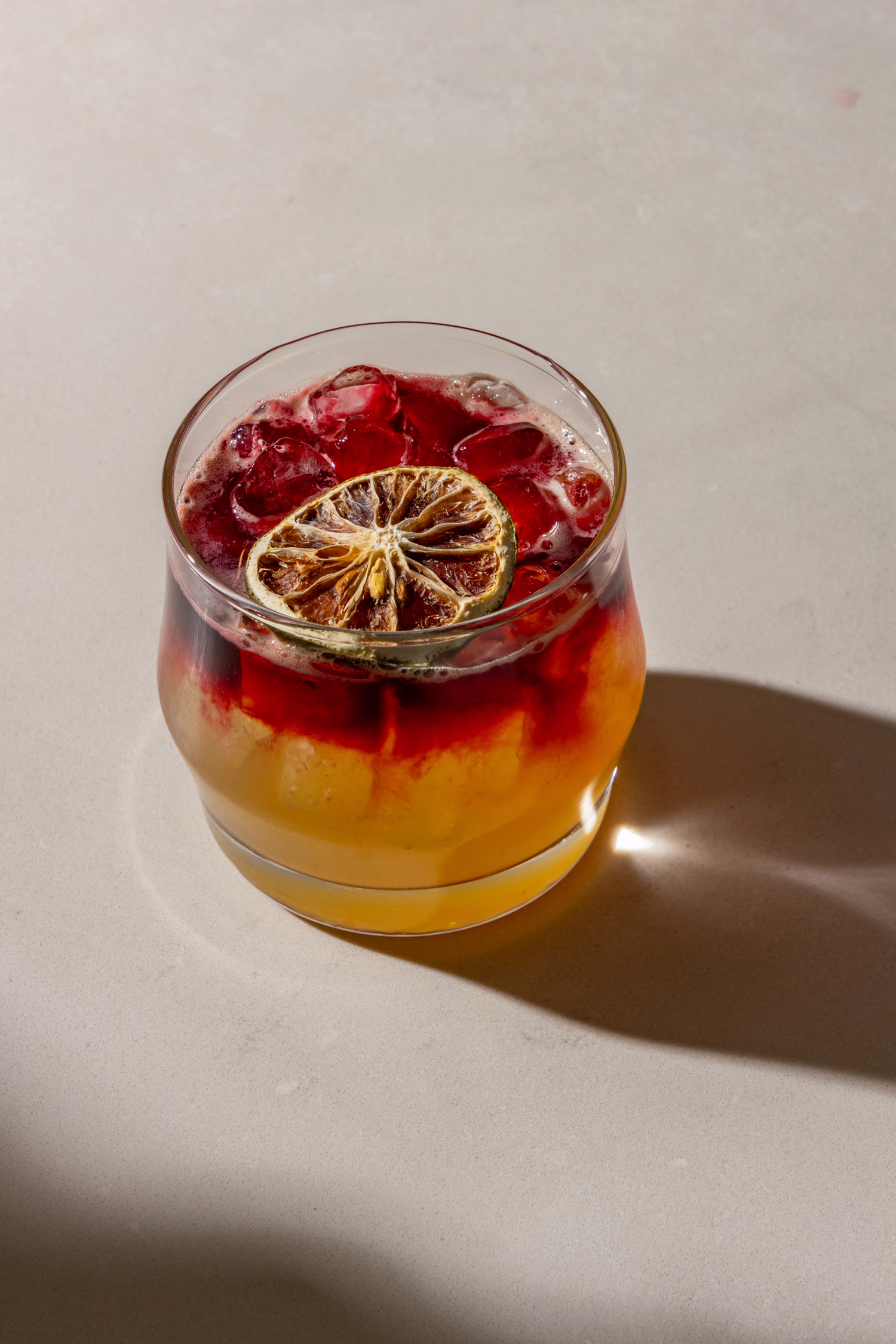 A layered red and gold cocktail with a dried citrus wheel at Mistora