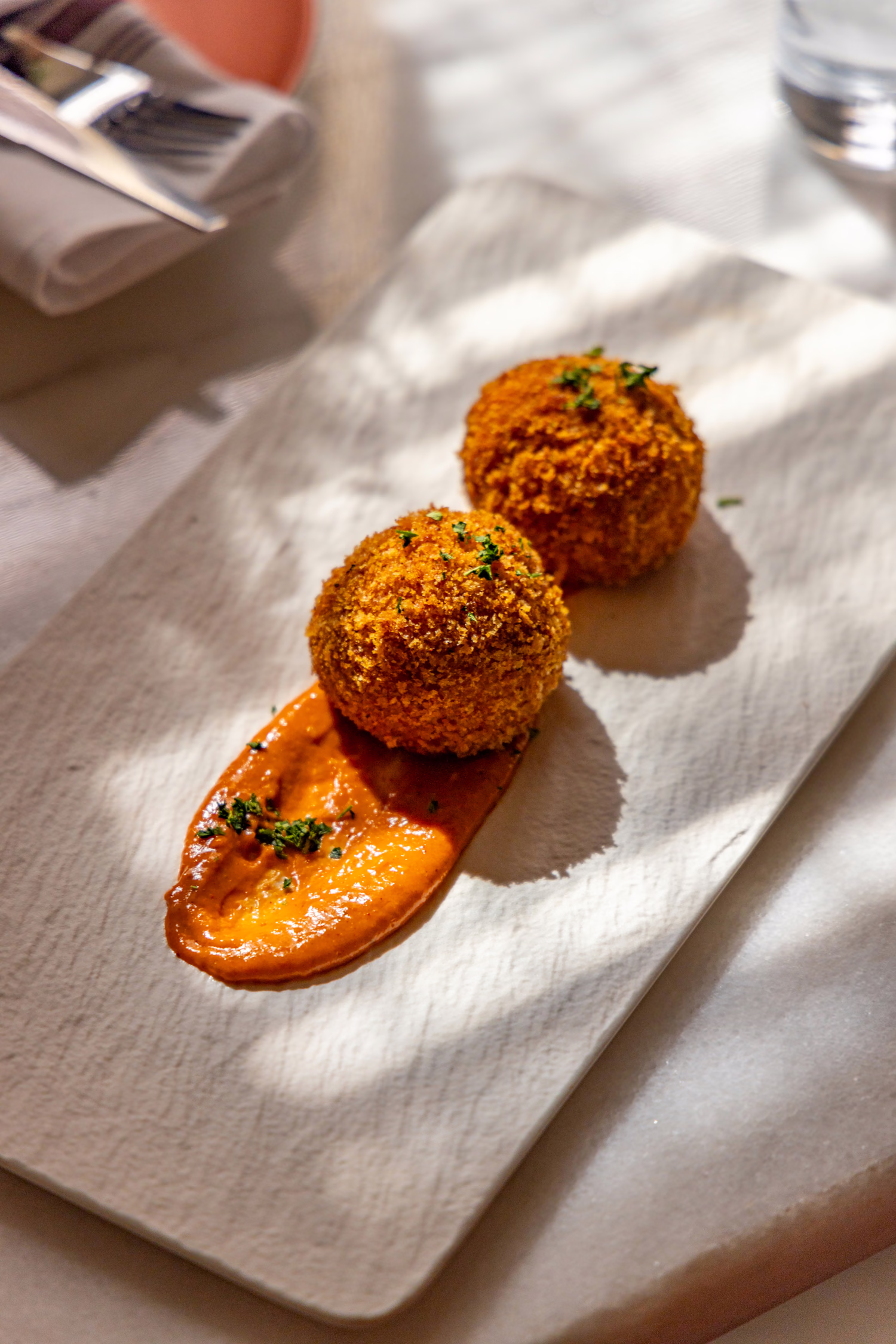 Two golden croquettes on a swipe of red sauce at Mistora