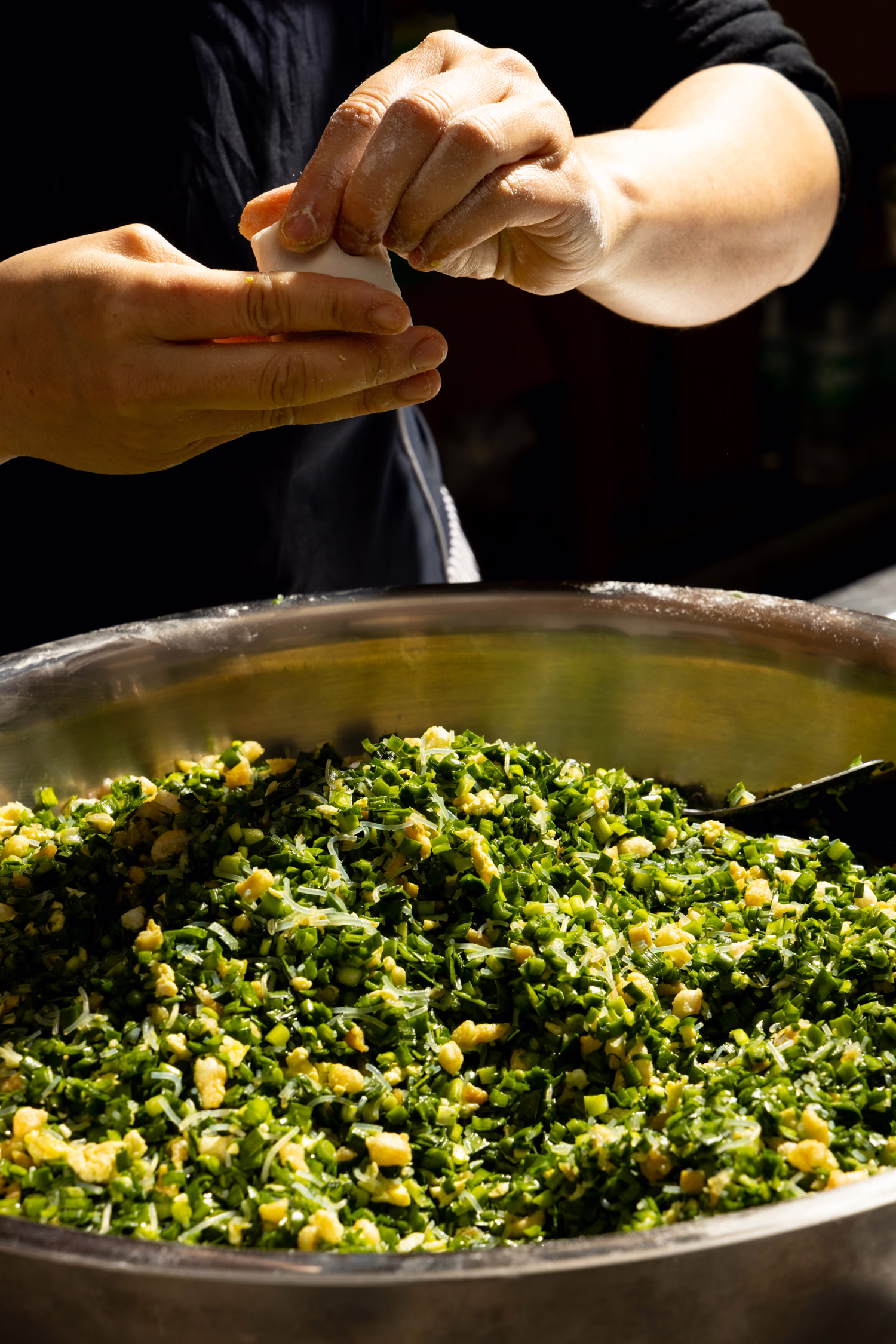 Hands folding a dumpling over a bowl of chive and egg filling at Dumpling Factory