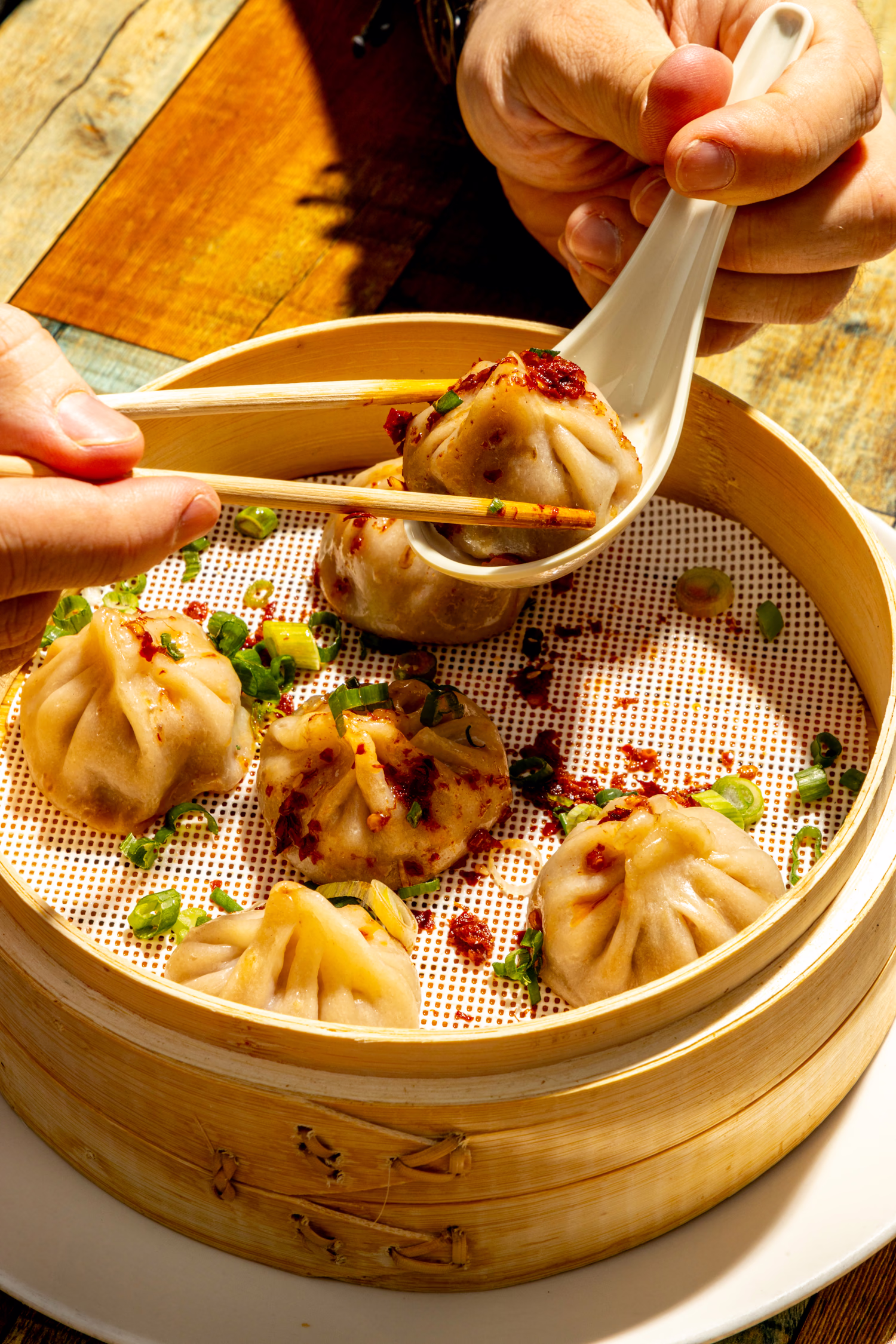 A soup dumpling lifted from the steamer with chopsticks and a spoon at Dumpling Factory