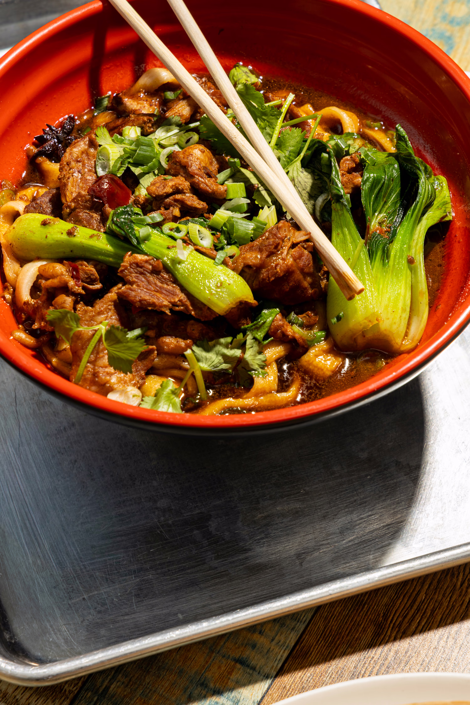 Braised beef noodle soup with bok choy in a red bowl at Dumpling Factory