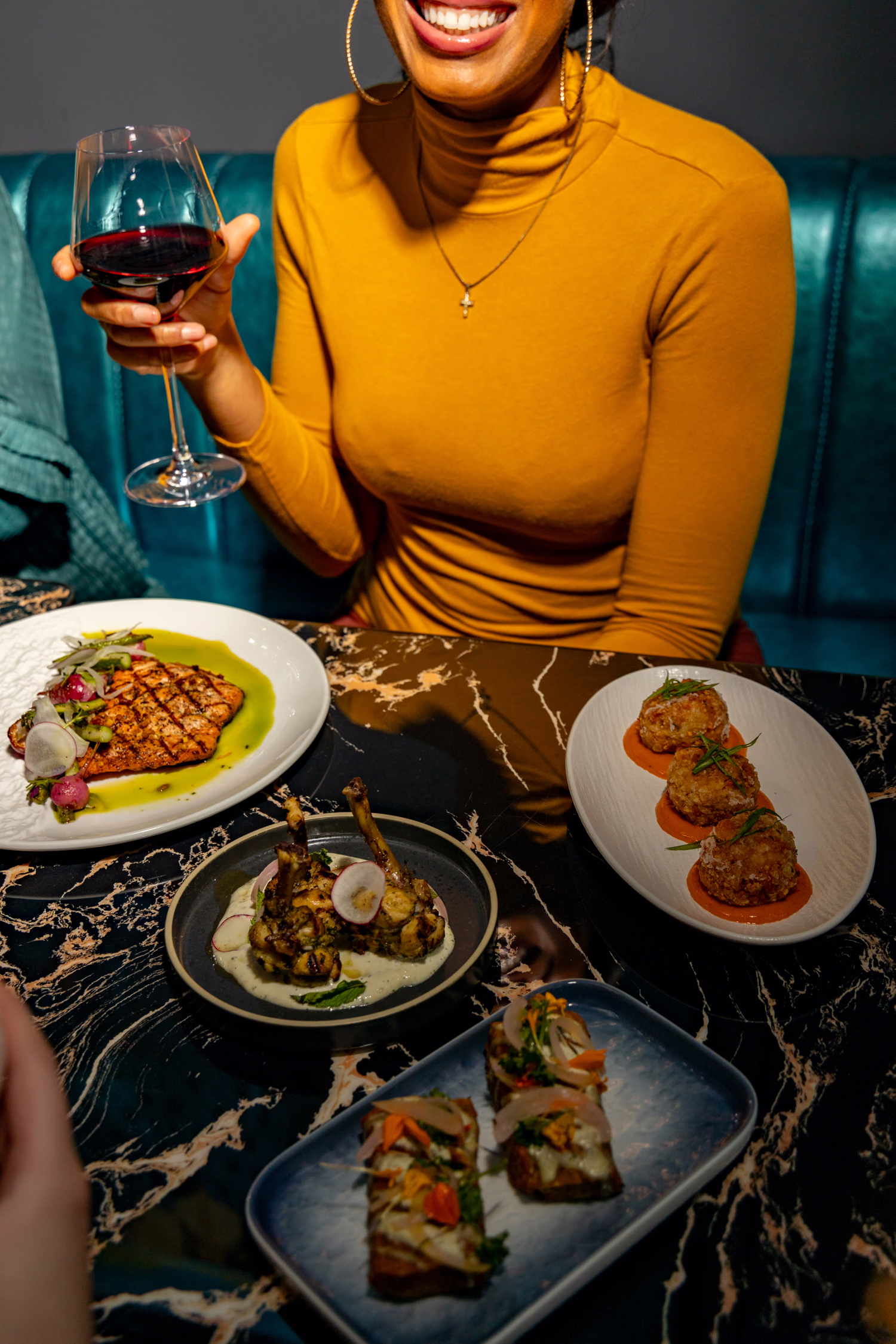 A guest with a glass of red wine at a marble table of shared plates at Siena