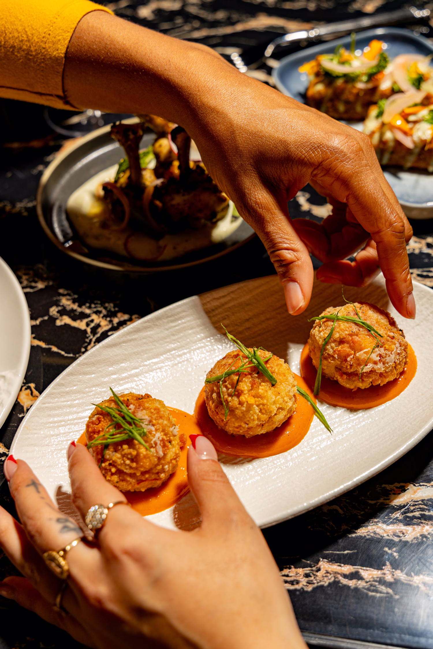 Hands reaching for croquettes on an orange sauce at Siena