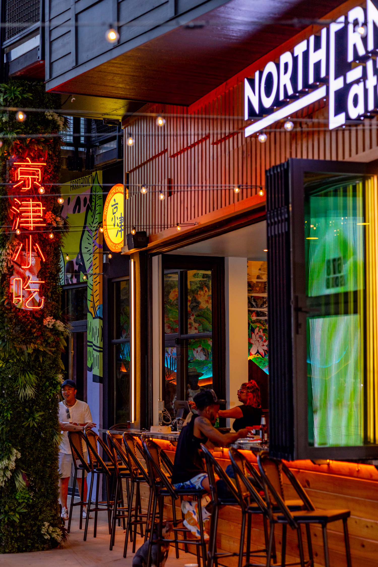 The storefront of Northern China Eatery at dusk, with neon signs and a patio counter