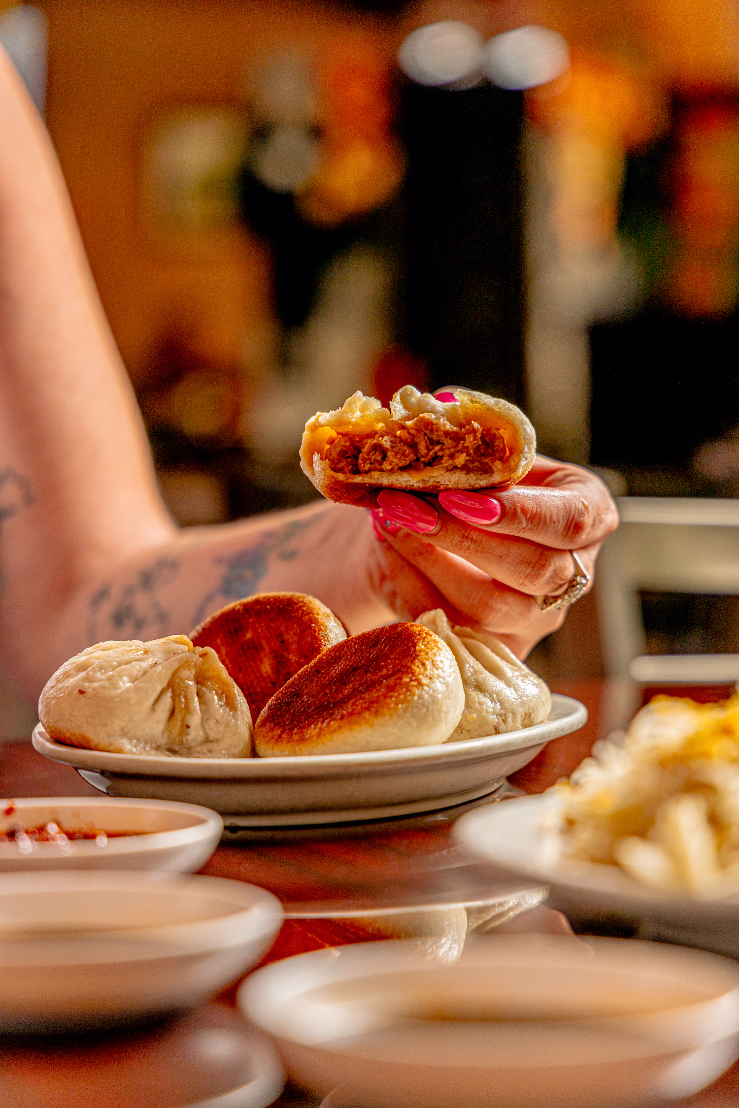 A hand holding a bitten pan-fried bun above a plate of buns at Northern China Eatery