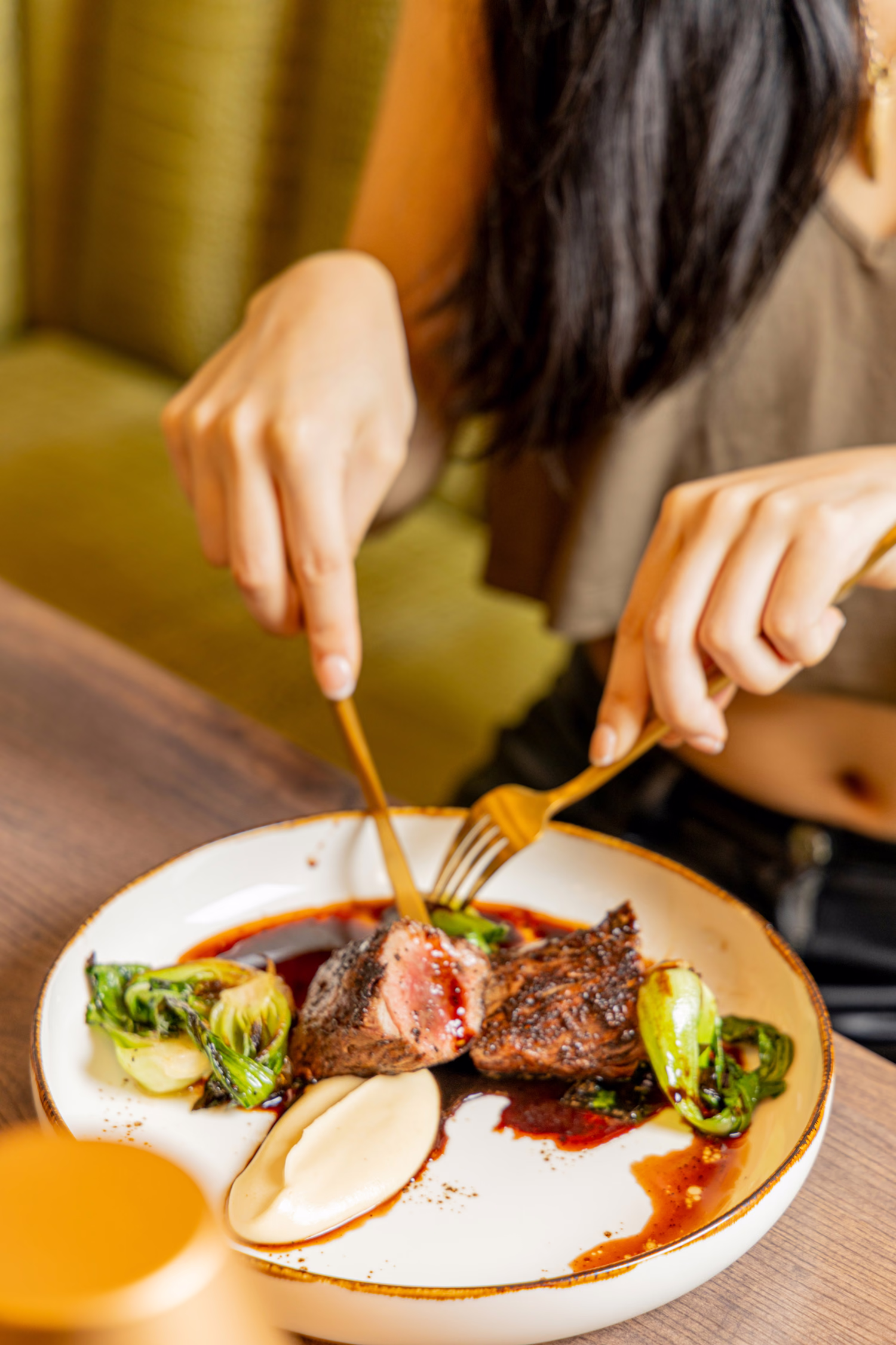 A guest cutting into steak with greens at a green booth at Auburn Angel