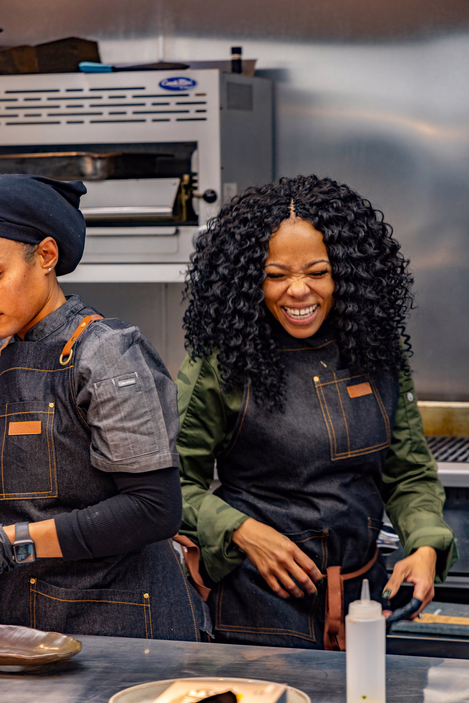 Two cooks laughing together on the kitchen line at Auburn Angel