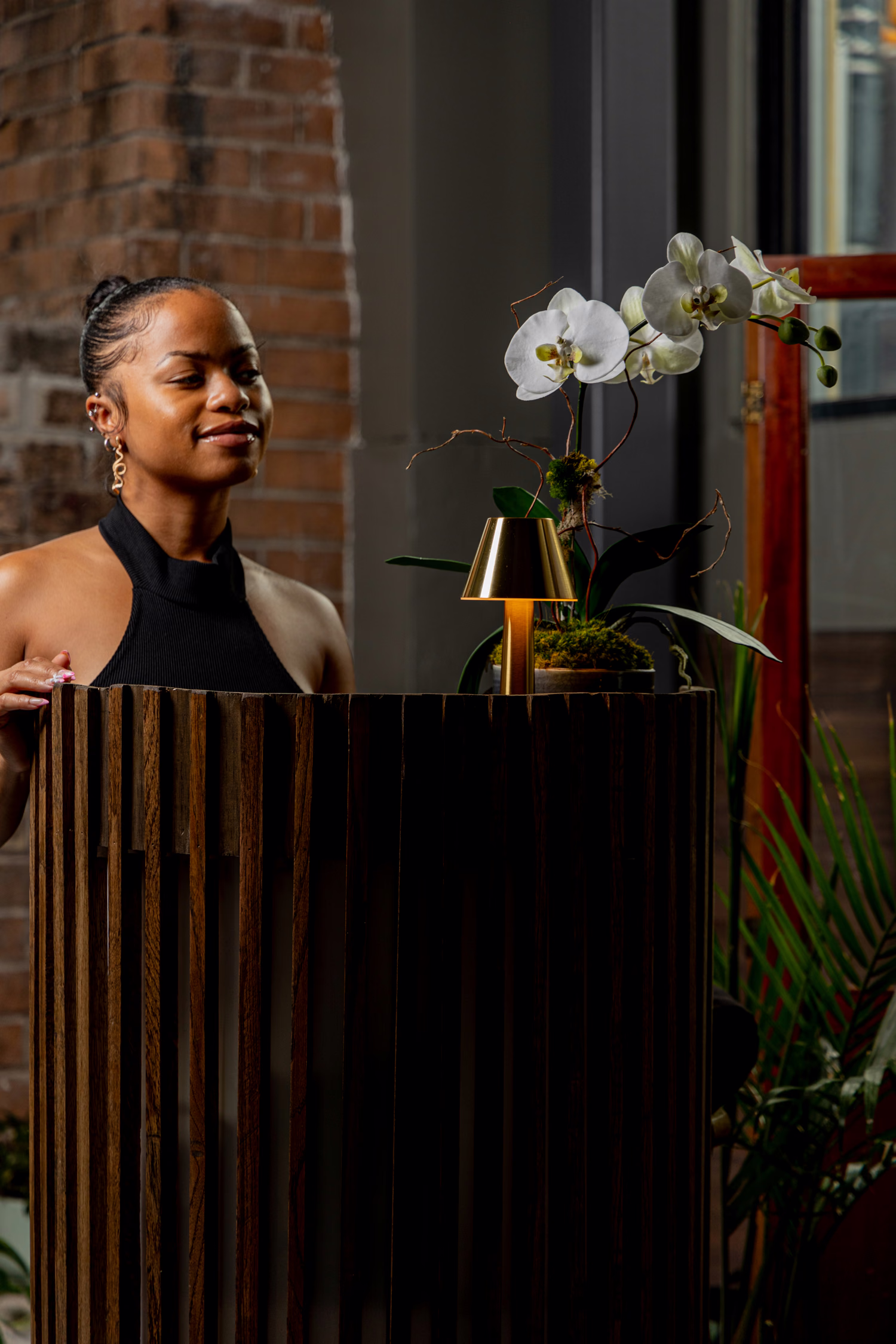 A host at the host stand beside an orchid and a brass lamp at Auburn Angel