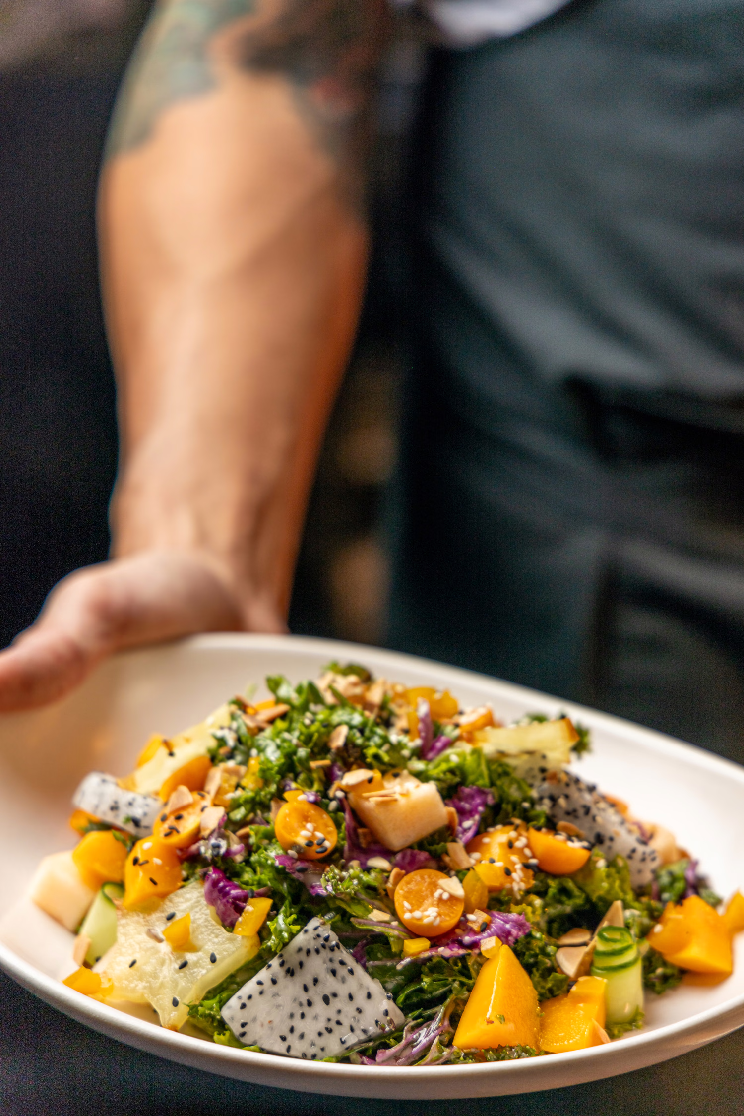 A cook setting down a salad with dragon fruit, mango and herbs at Auburn Angel
