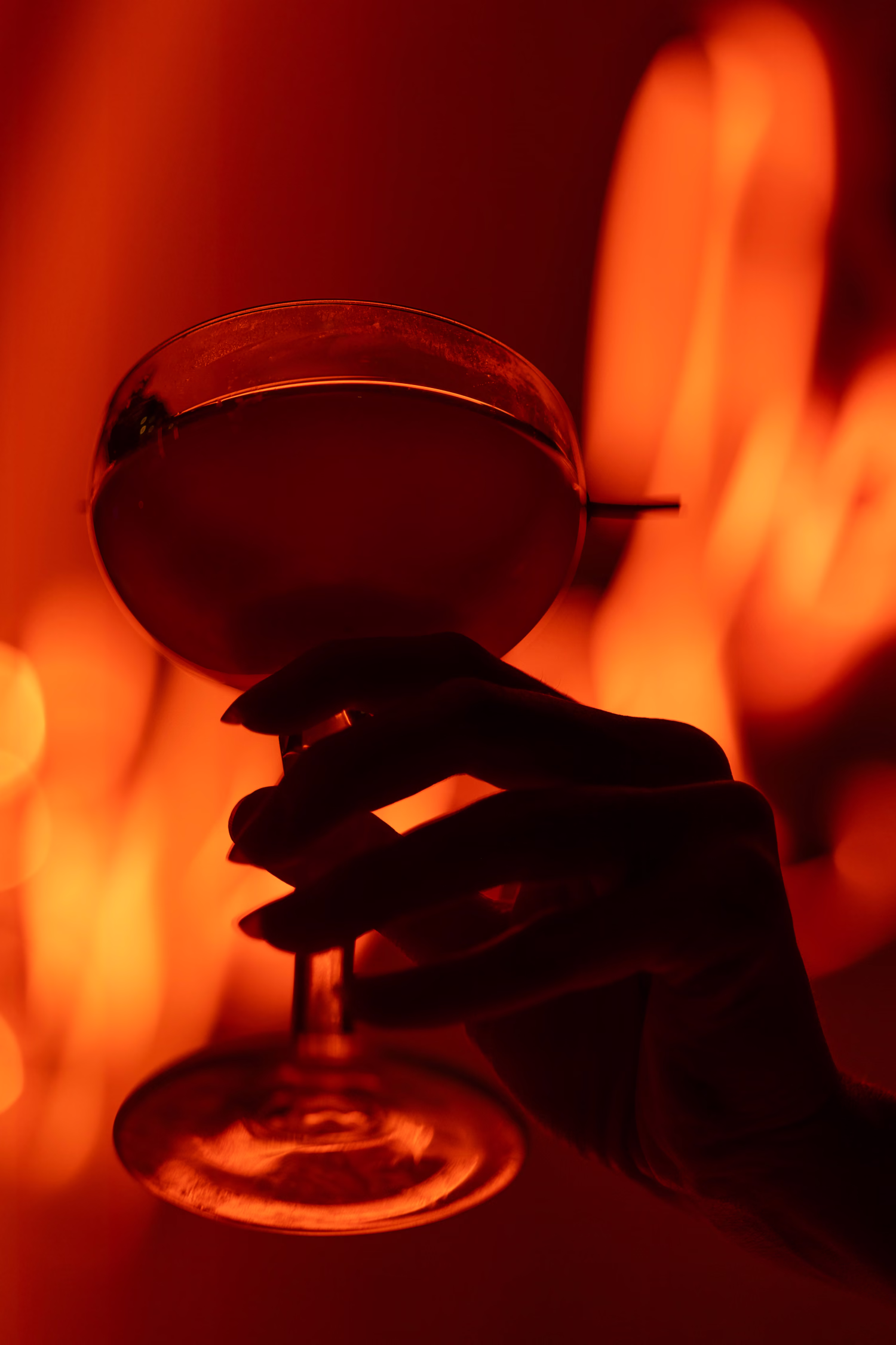 A hand holding a coupe glass silhouetted in red light at Verdure