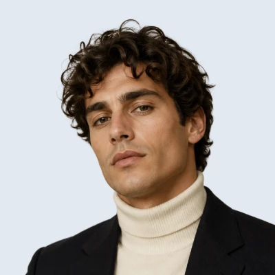 Portrait of a person with curly dark hair wearing a blazer and turtleneck.