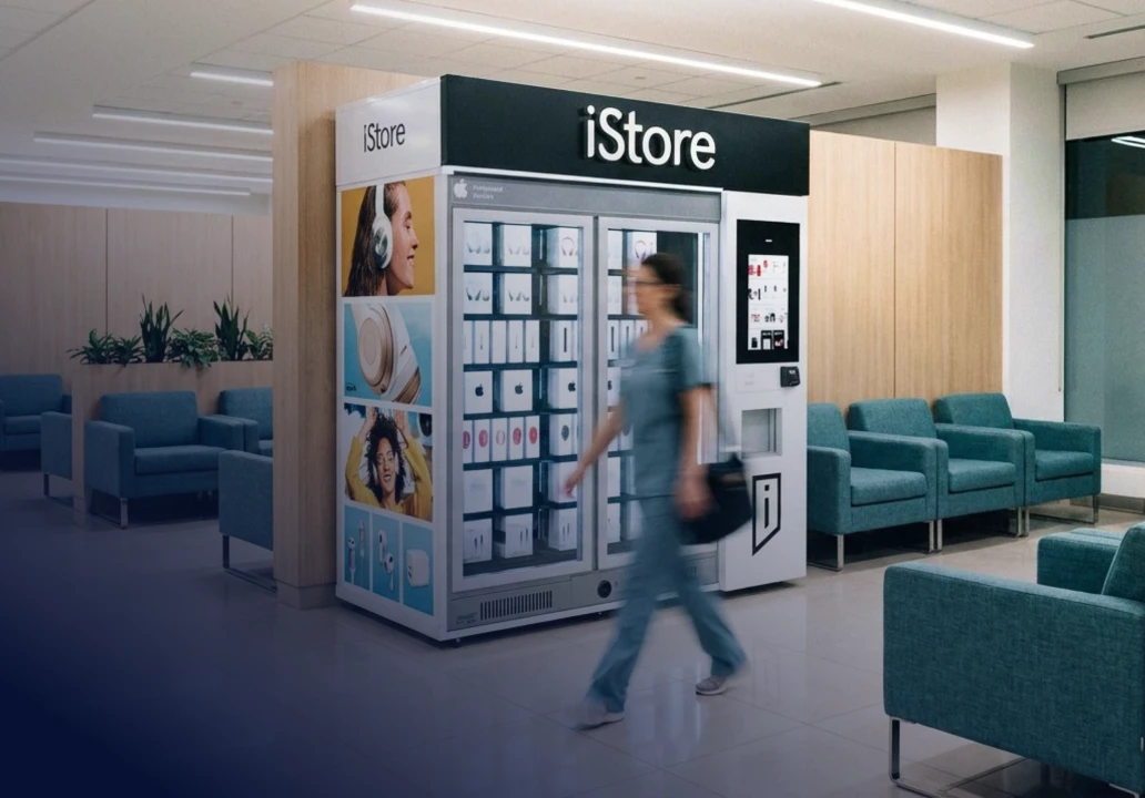 Traveler passing an iStore kiosk beside teal lounge chairs.
