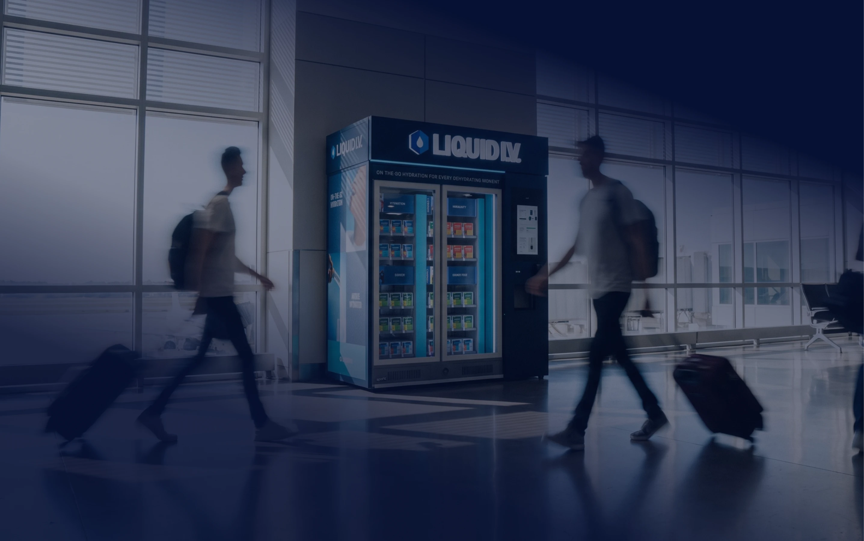 Travelers with rolling suitcases walking past a Liquid I.V. automated retail kiosk in an airport terminal.