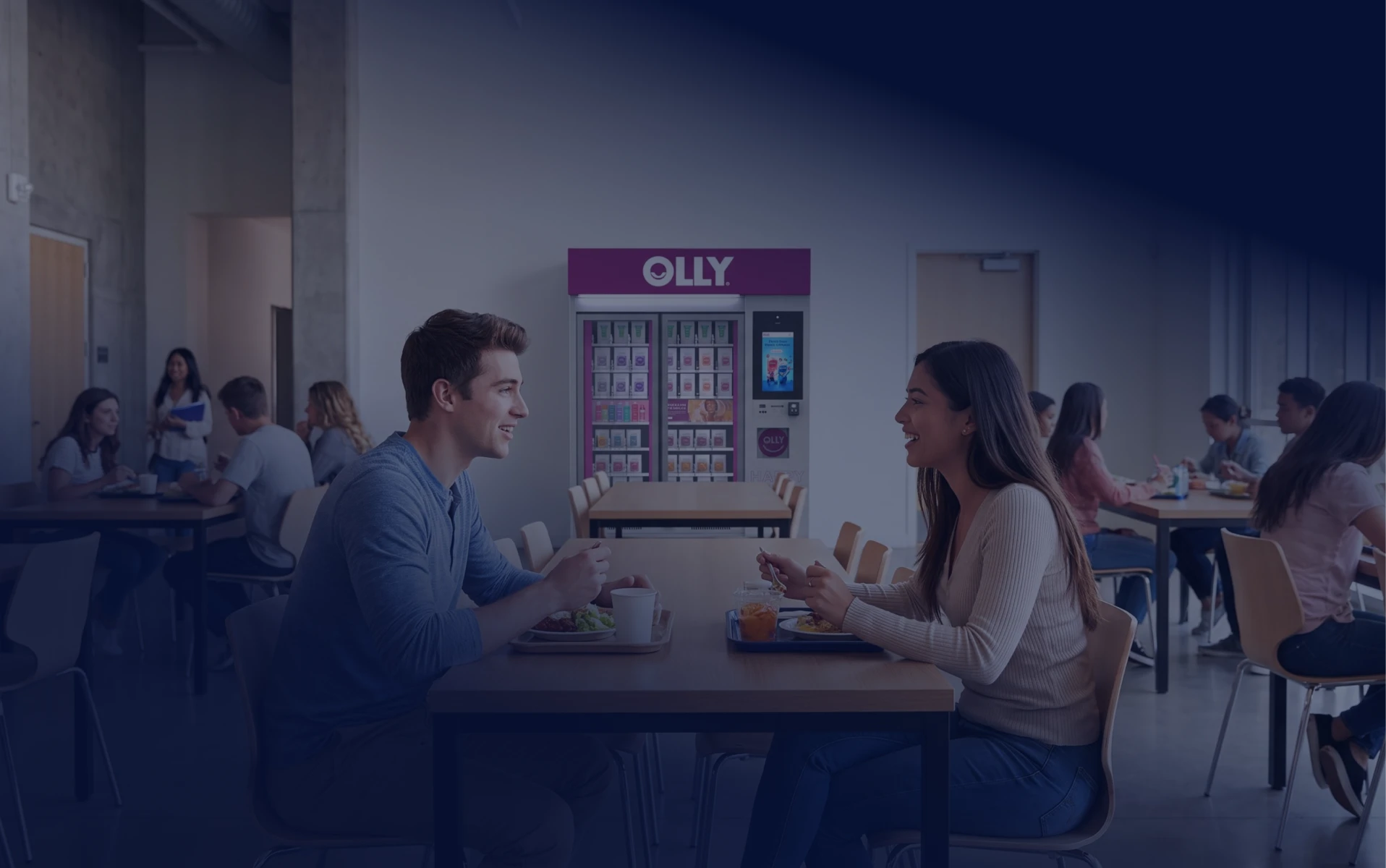 Students eating and talking at a table near an OLLY kiosk.