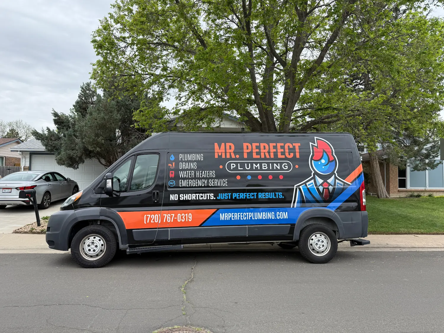 Black service van for Mr. Perfect Plumbing parked on a residential street with green trees and houses in the background, featuring text advertising plumbing, drains, water heaters, emergency service, a phone number, and website.