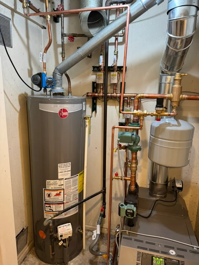 A home utility room with a Rheem water heater on the left and a furnace on the right, interconnected with copper pipes and ventilation ducts.