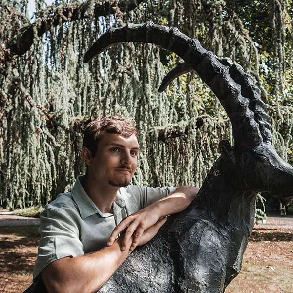 Image of Xavier Cubbin leaning against a metal goat statue in a park.