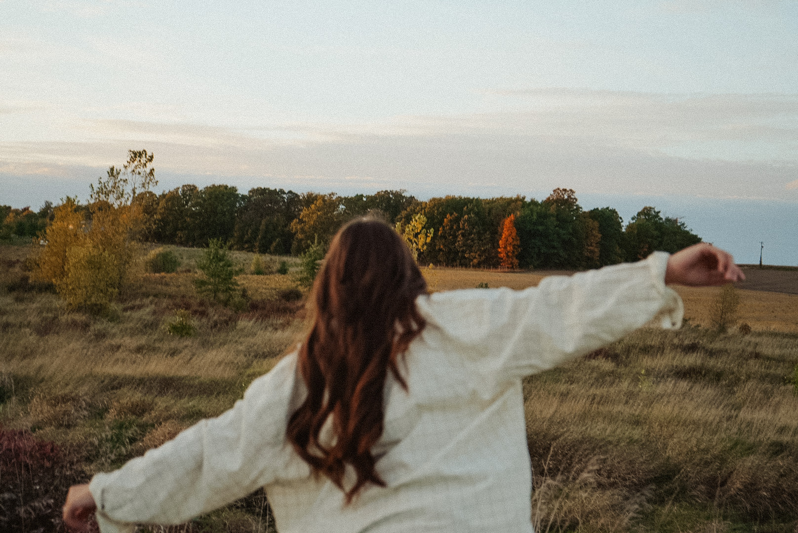 Woman standing in an open field with her arms spread wide.