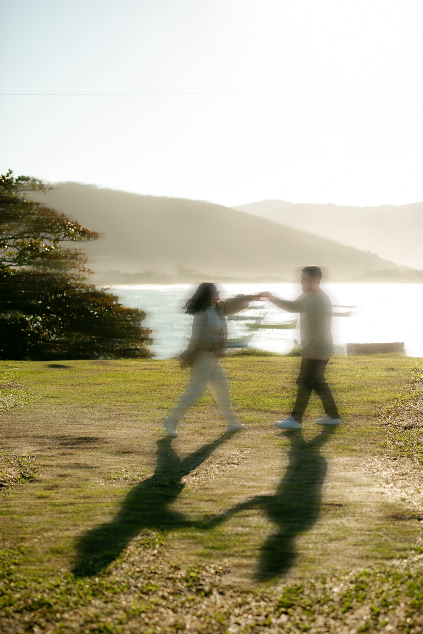 Two people holding hands beside a sunlit lake