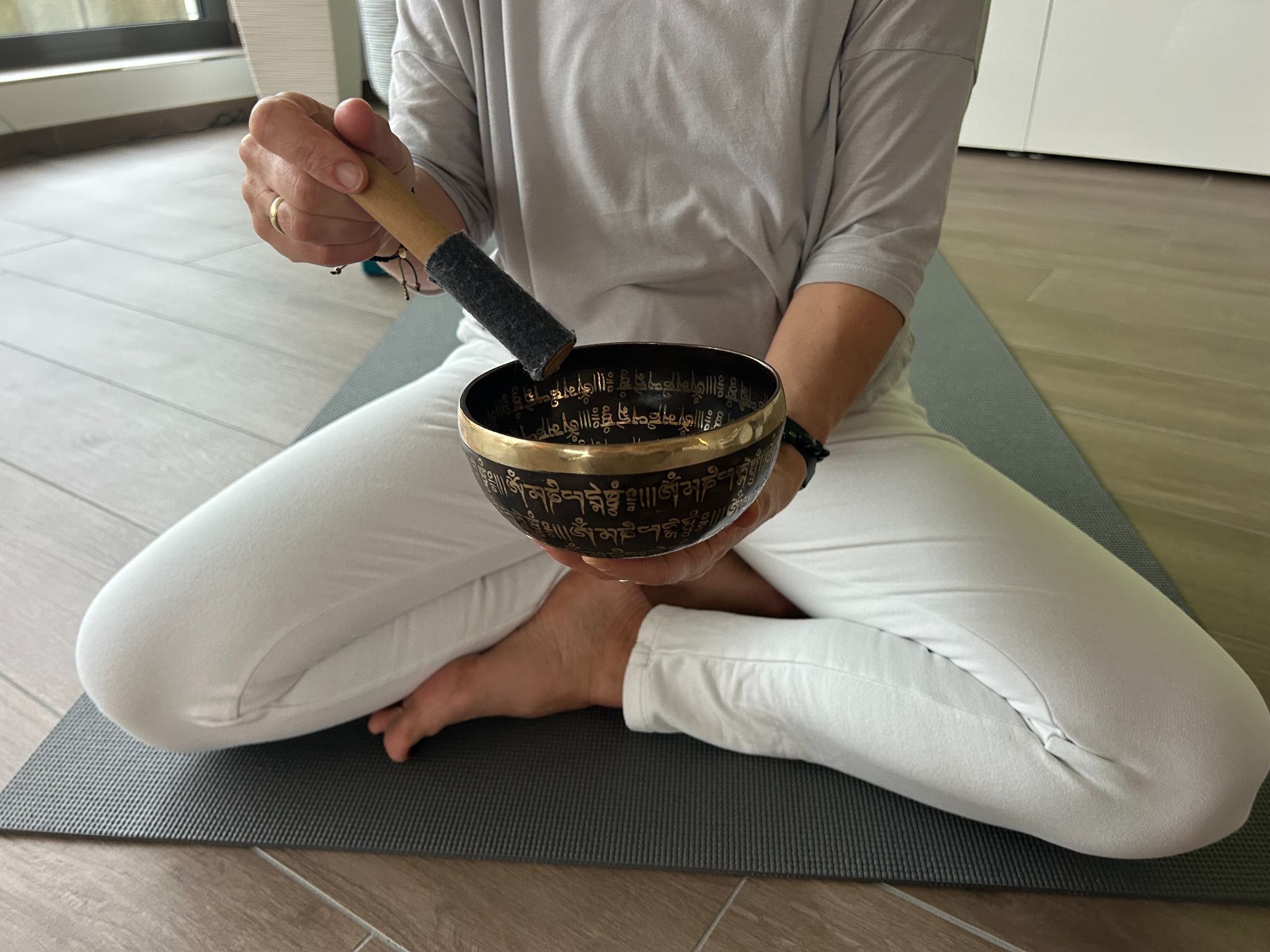 Person holding a singing bowl while seated on a yoga mat