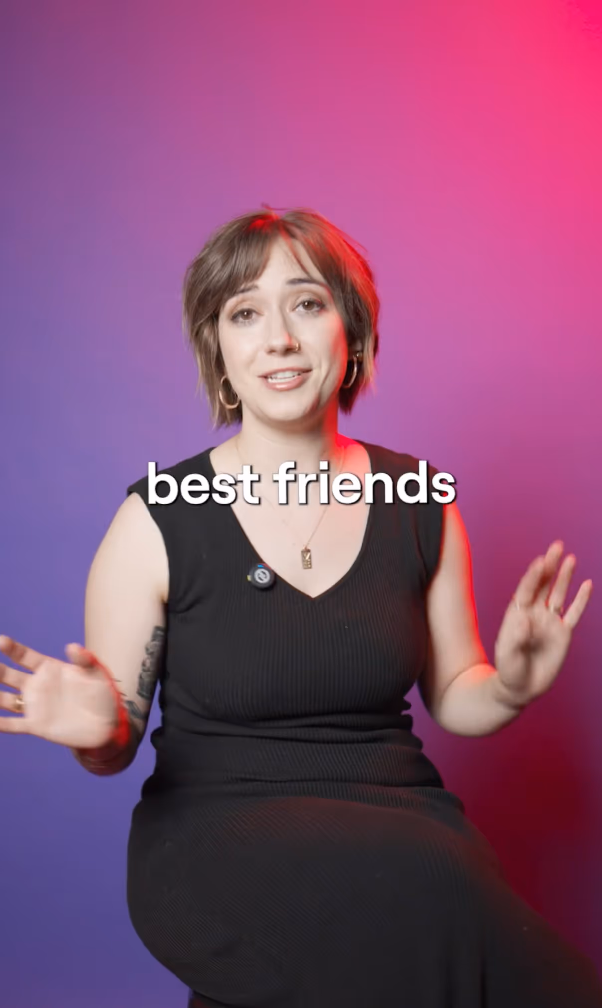 Person with short brown hair wearing a black sleeveless dress, smiling and gesturing with hands against a purple and pink gradient background with text 'best friends'.
