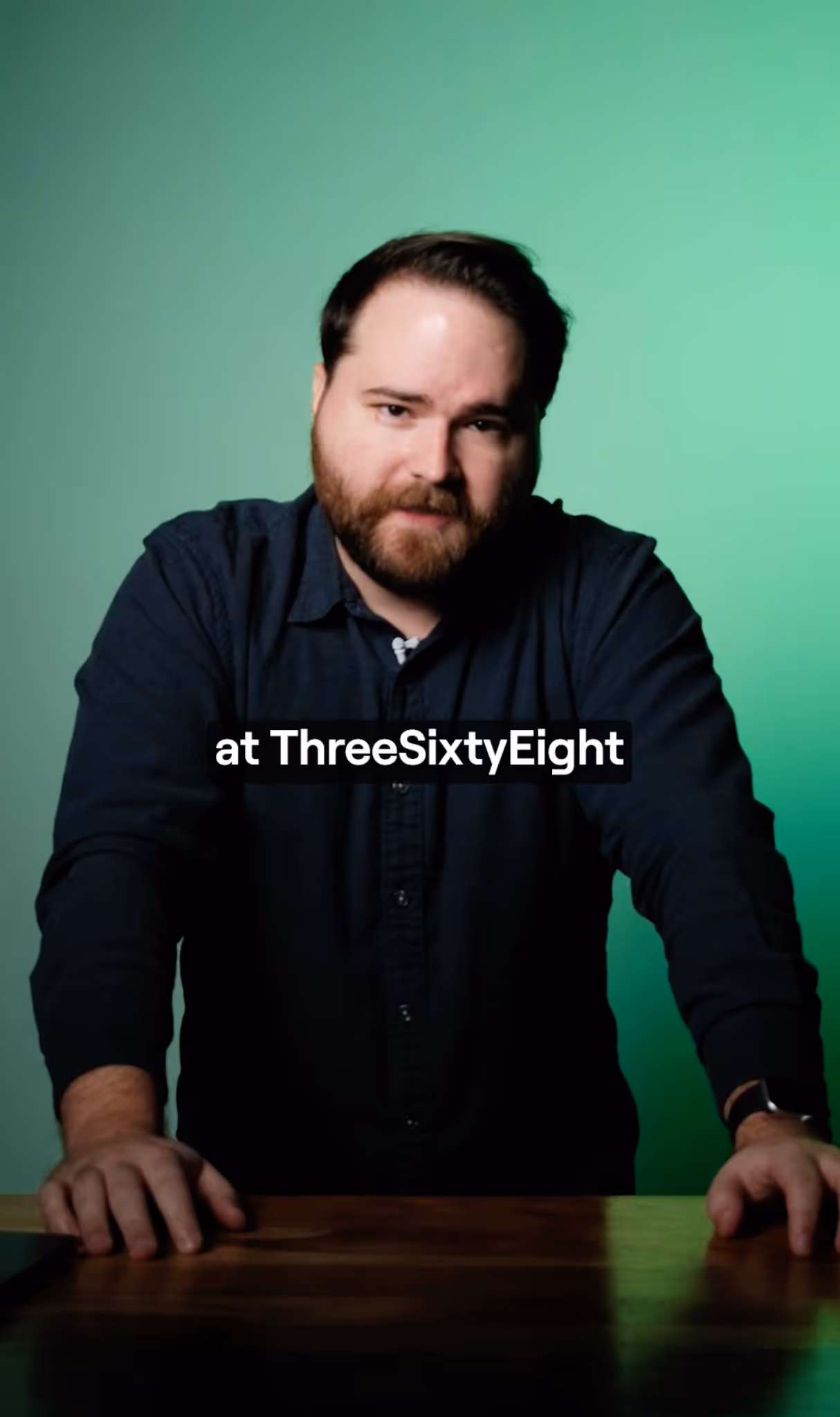 Man with beard and dark shirt leaning on a wooden table against a green background with text overlay 'at ThreeSixtyEight'.