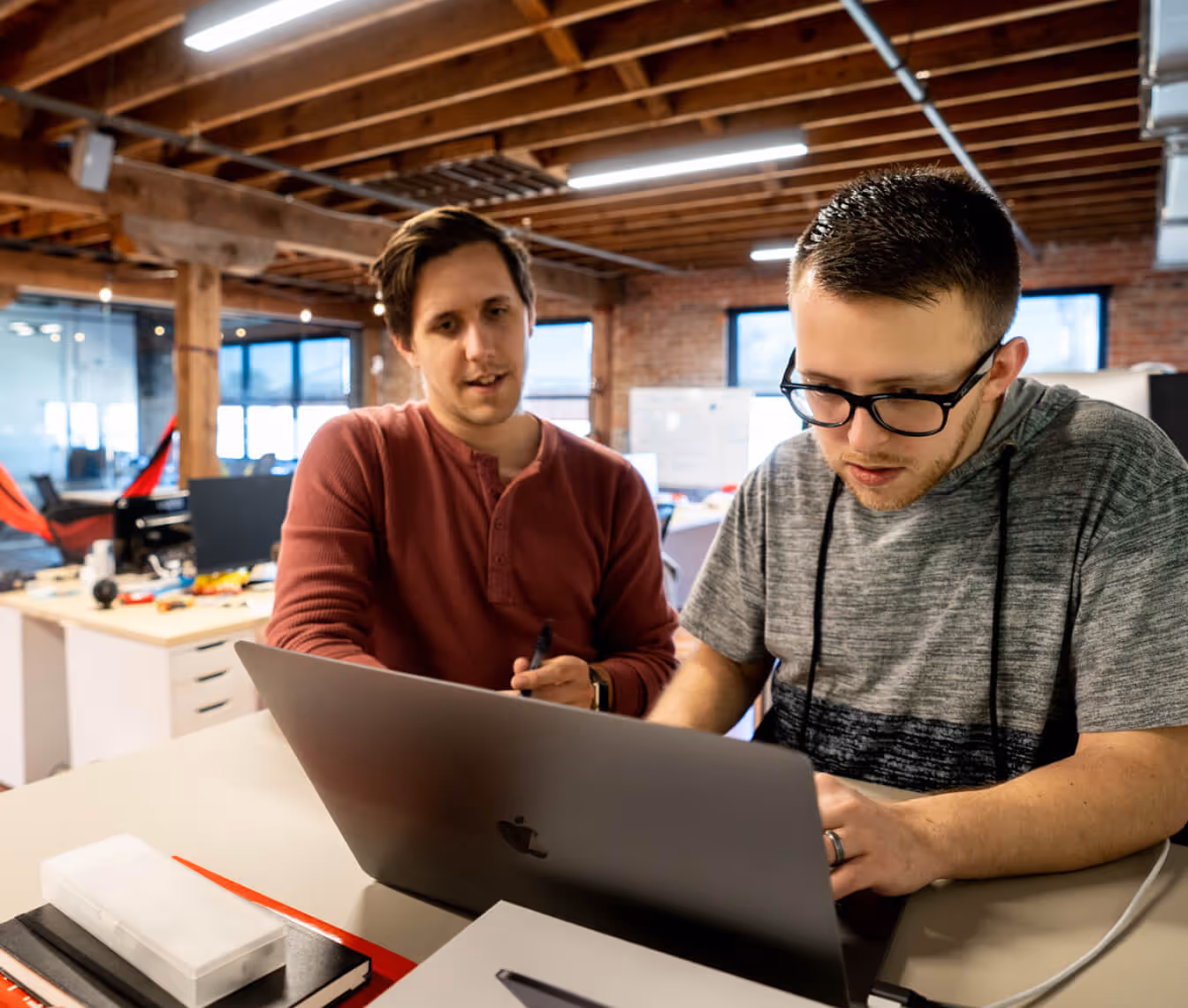 Corey and Tim collaborate while working on a laptop in a modern office with exposed wooden beams.
