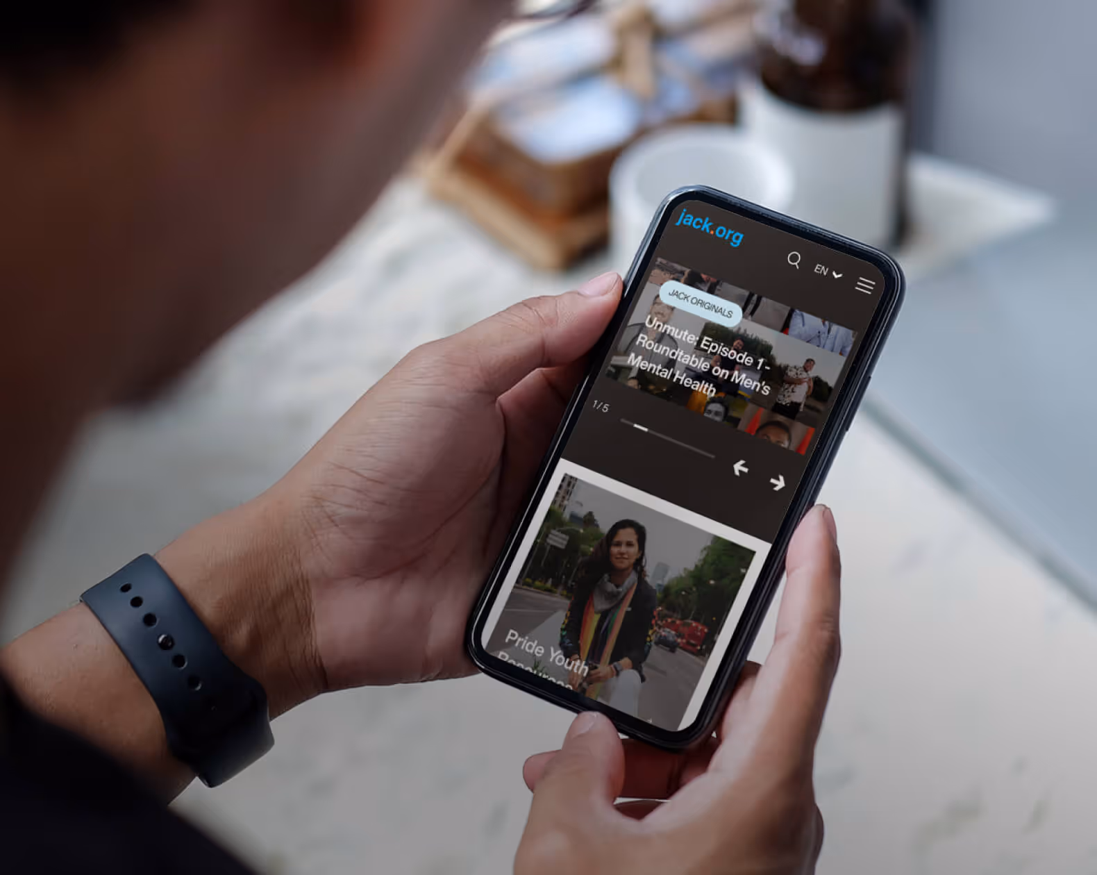 Person holding a smartphone displaying the jack.org website featuring articles on mental health and pride youth.
