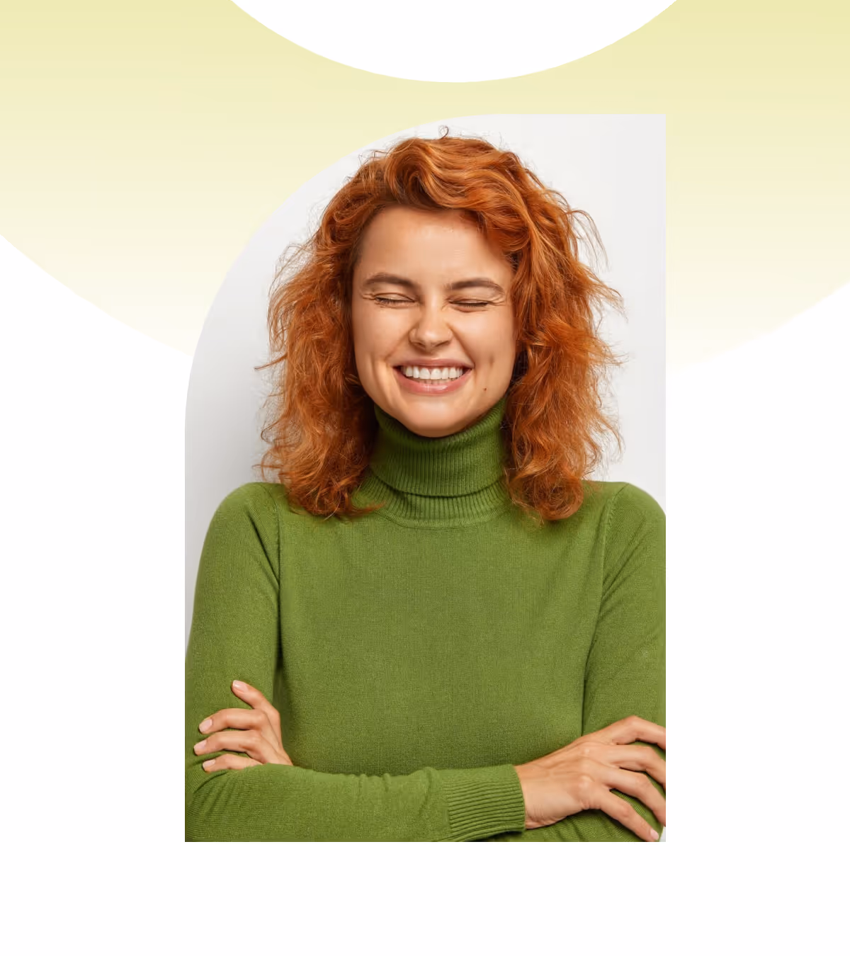 Smiling woman with curly red hair wearing a green turtleneck sweater with arms crossed and eyes closed.