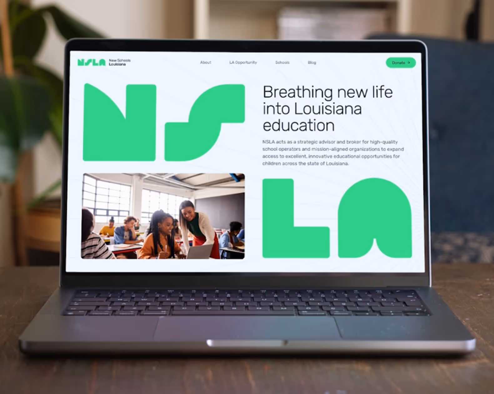 Laptop screen displaying a New Schools Louisiana website with a headline about improving education and a photo of a teacher helping students in a classroom.