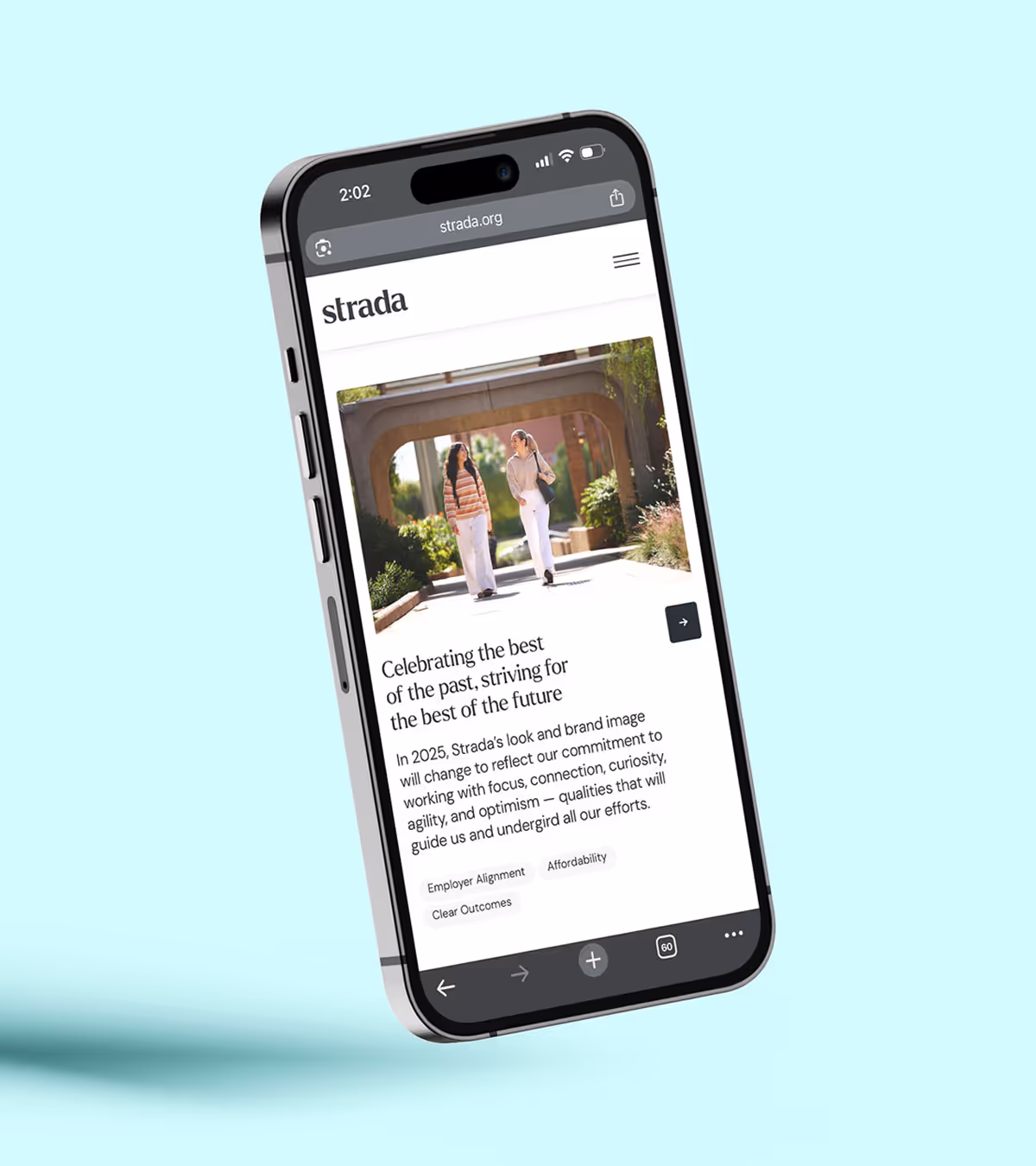 Smartphone displaying a webpage from strada.org about the brand's 2025 look and commitment to focus, connection, curiosity, agility, and optimism, with an image of two women walking outdoors under an archway.