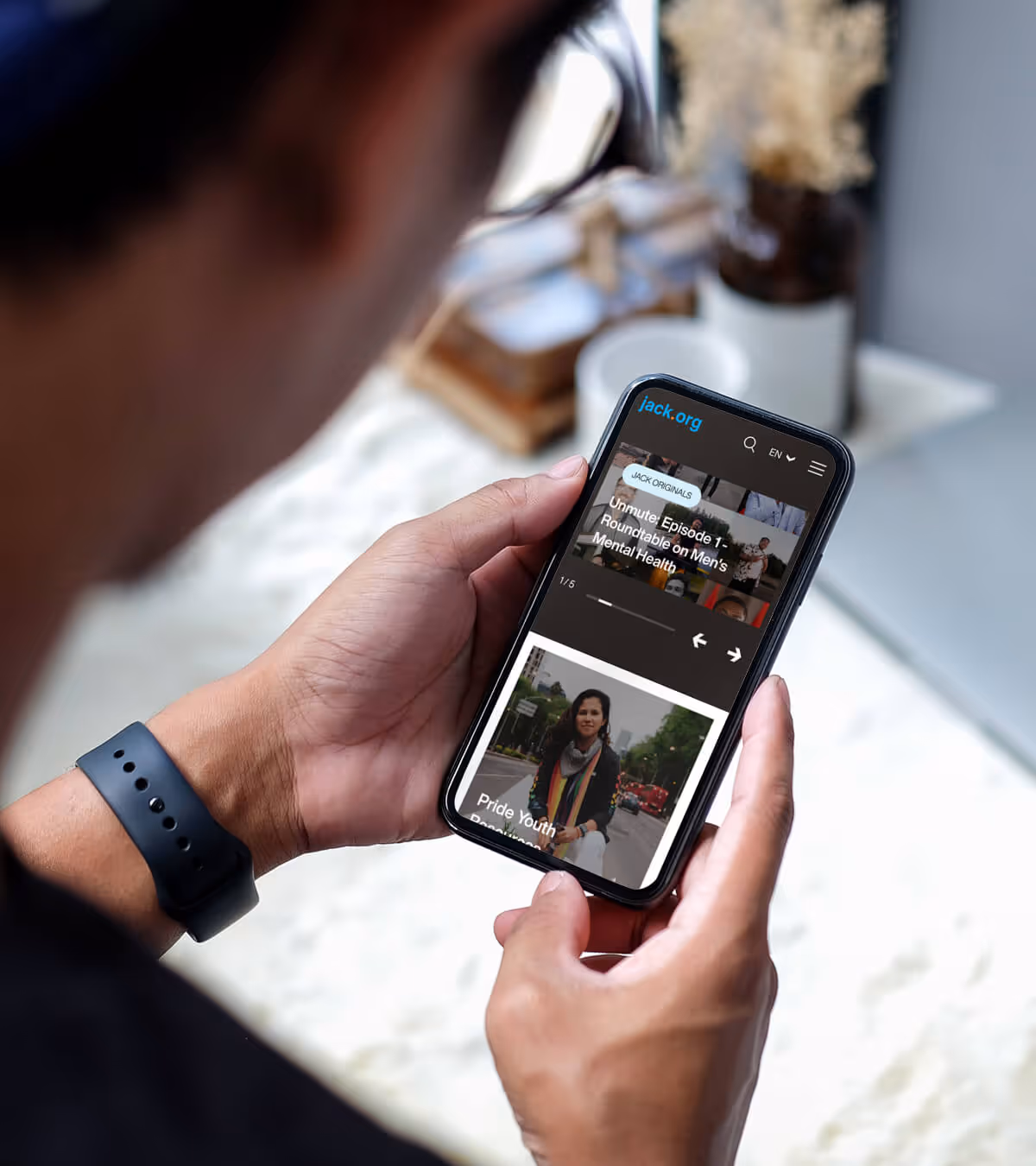 Person holding a smartphone displaying the jack.org website with articles on men's mental health and pride youth resources.