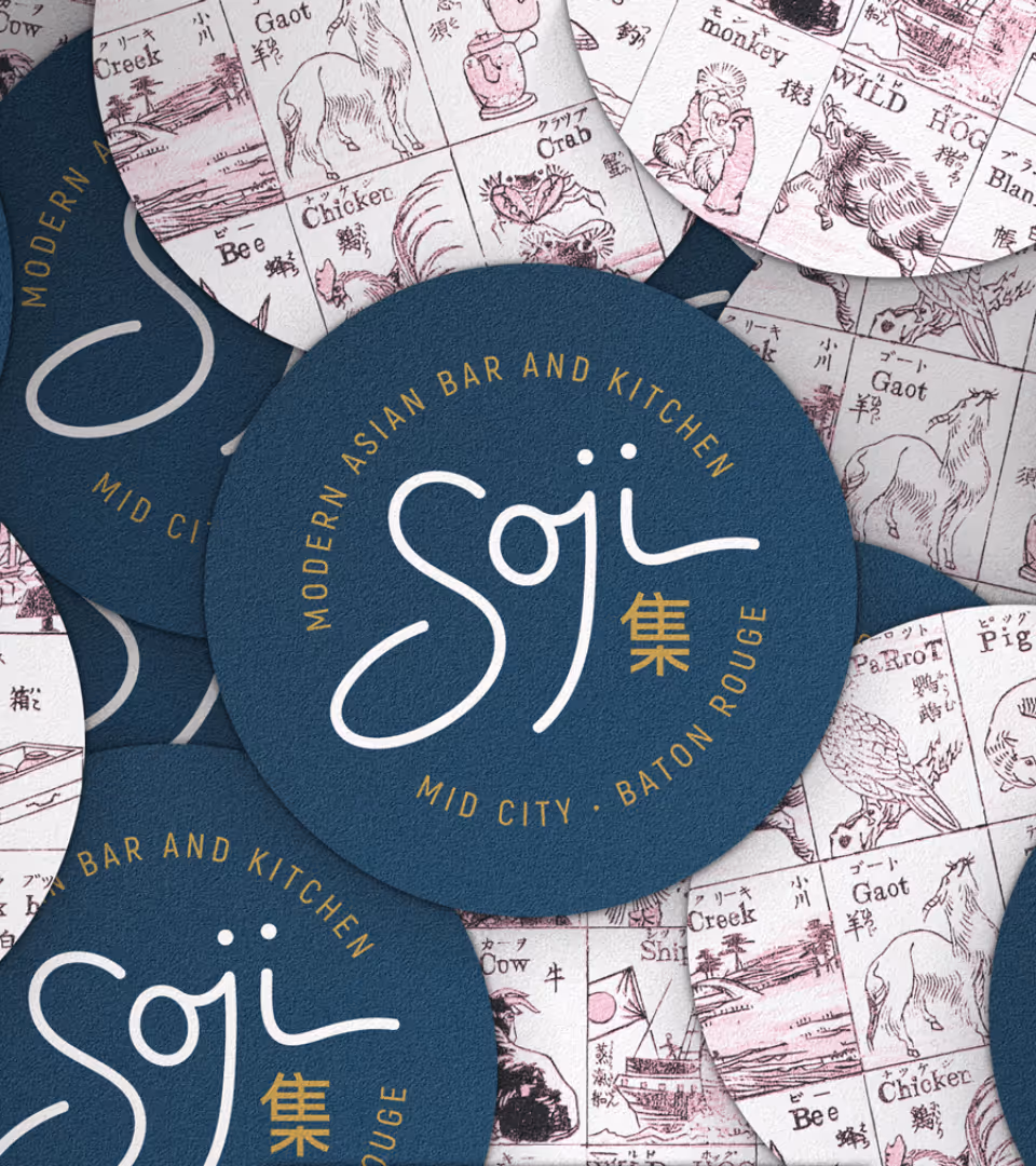 Blue circular coasters with gold text stating 'Soji' and 'Modern Asian Bar and Kitchen, Mid City, Baton Rouge' overlaid on vintage-style animal illustration papers.