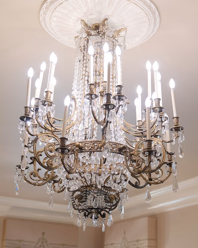 Elegant vintage chandelier with ornate metal arms and hanging crystal prisms, lit with candle-shaped bulbs.