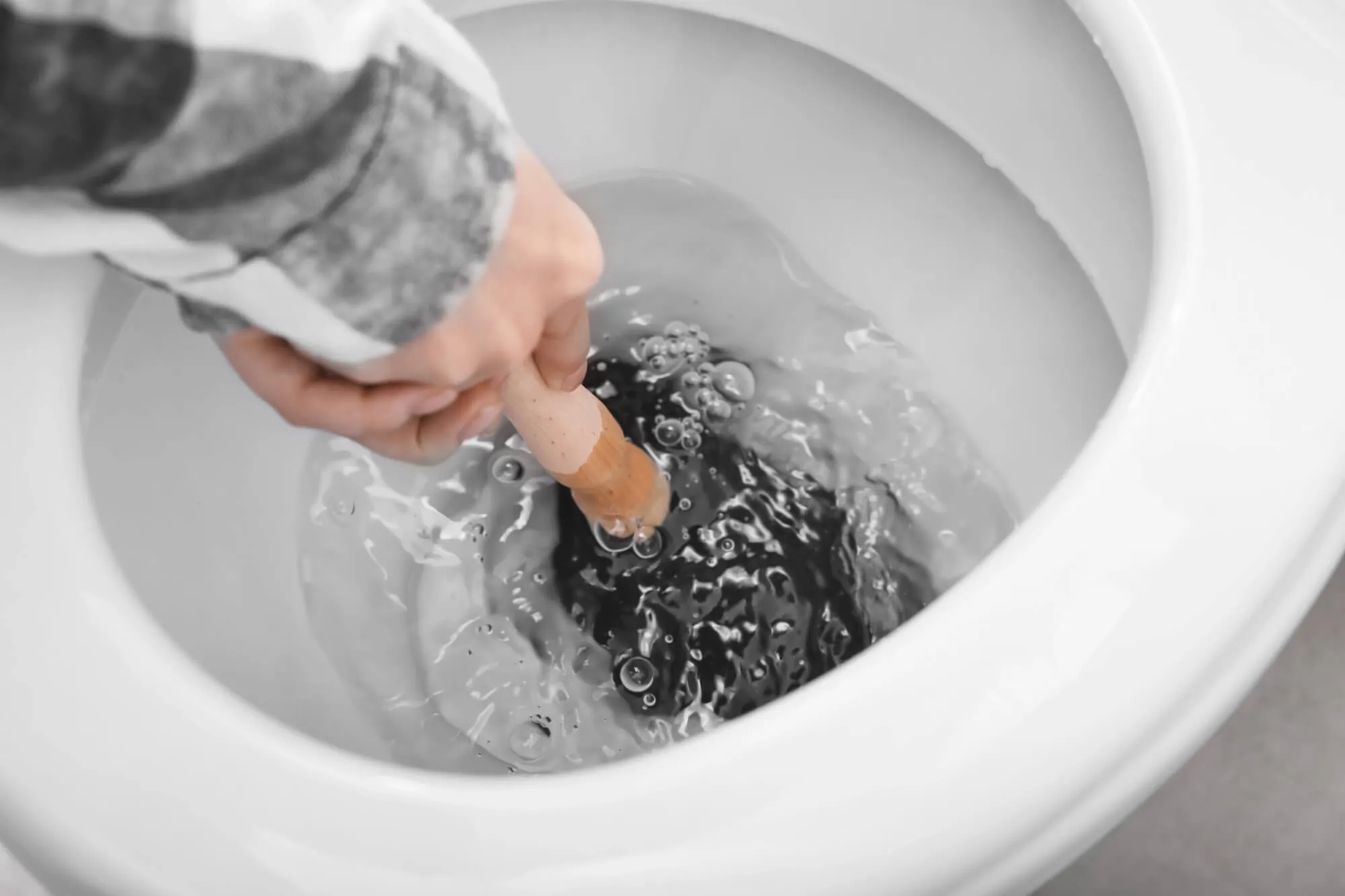Gloved hand clearing a clogged toilet drain