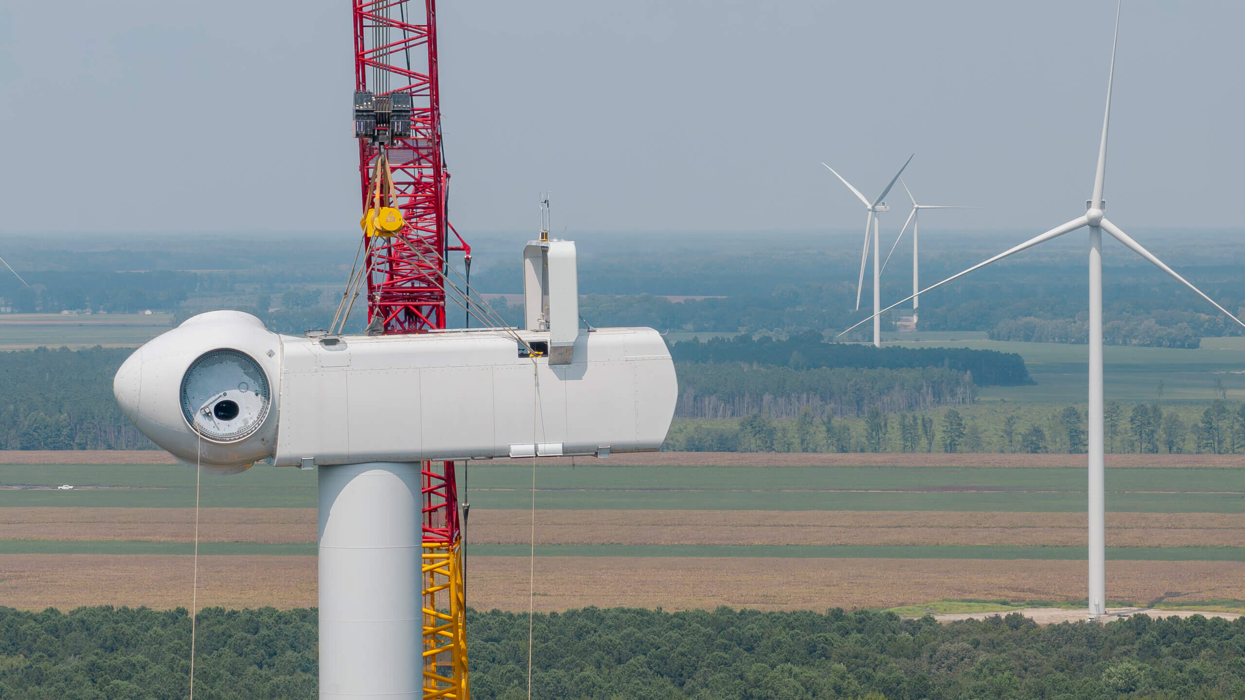 Green John Deere agricultural machine in a field with wind turbines against a clear blue sky.