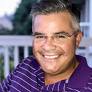 Smiling middle-aged man with short gray hair and glasses wearing a purple striped shirt outdoors at night.