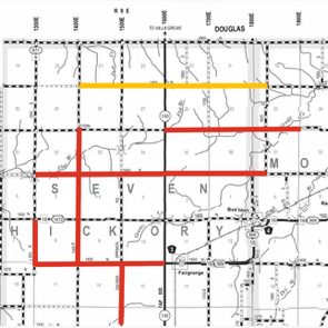Black-and-white map showing a grid of roads labeled with numbers and letters, with two colored lines: a yellow horizontal line near the top and a red line forming a rectangular loop and a vertical extension near the bottom left center, highlighting specific routes in the region.