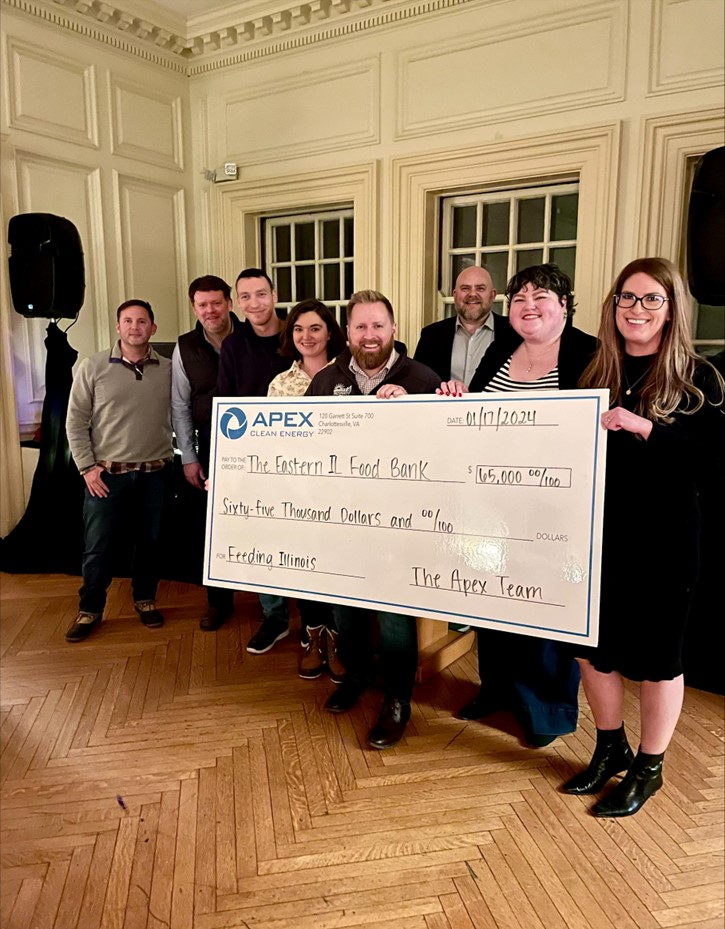 Group of eight people standing indoors holding a large check from Apex Clean Energy for sixty-five thousand dollars made out to The Eastern IL Food Bank, dated 01/17/2024, signed by The Apex Team, for Feeding Illinois.