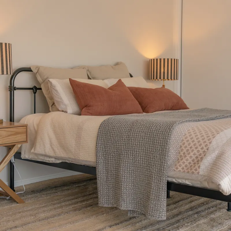 The bedroom, the bed made up with linen and a wall lamp either side