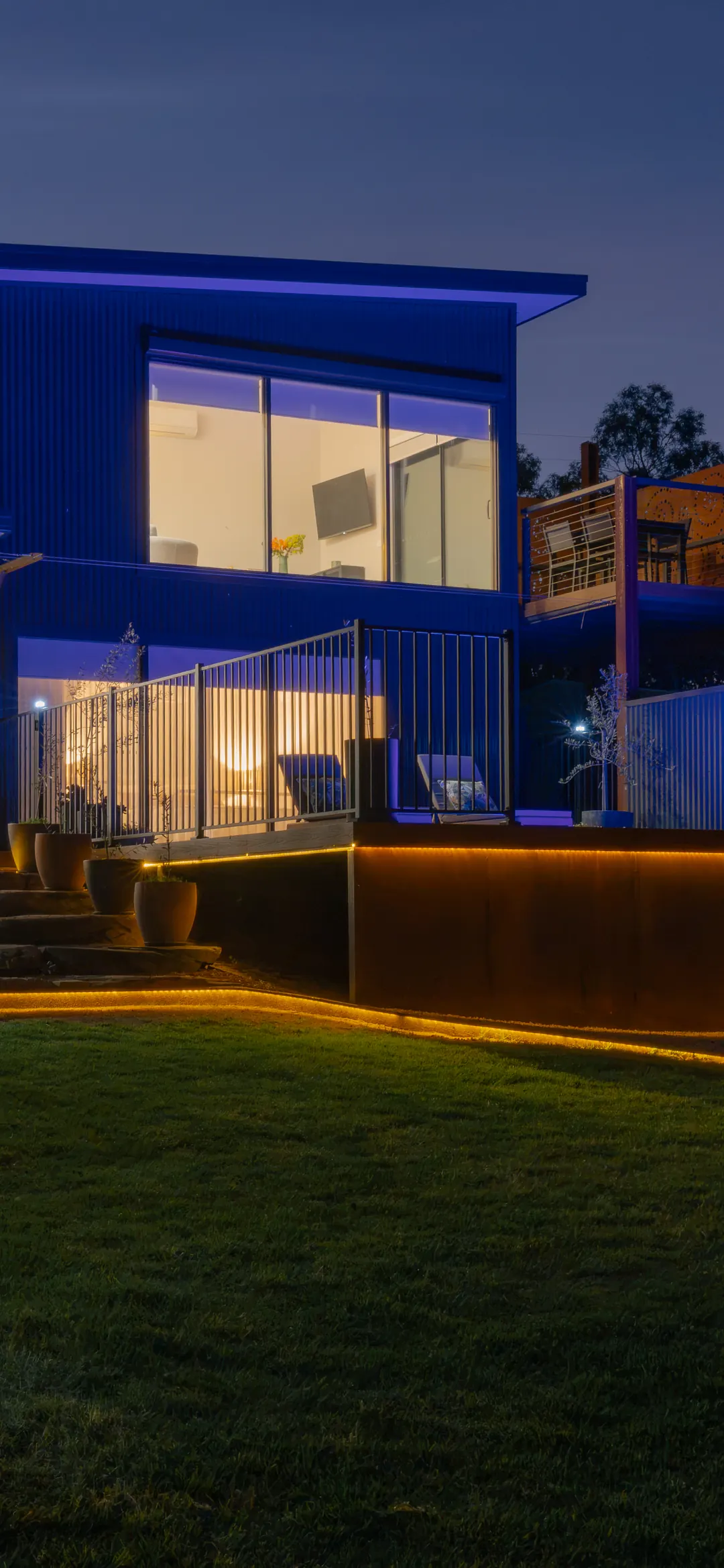The two-storey accommodation at dusk, lit inside and out, on the lawn under a deep blue sky