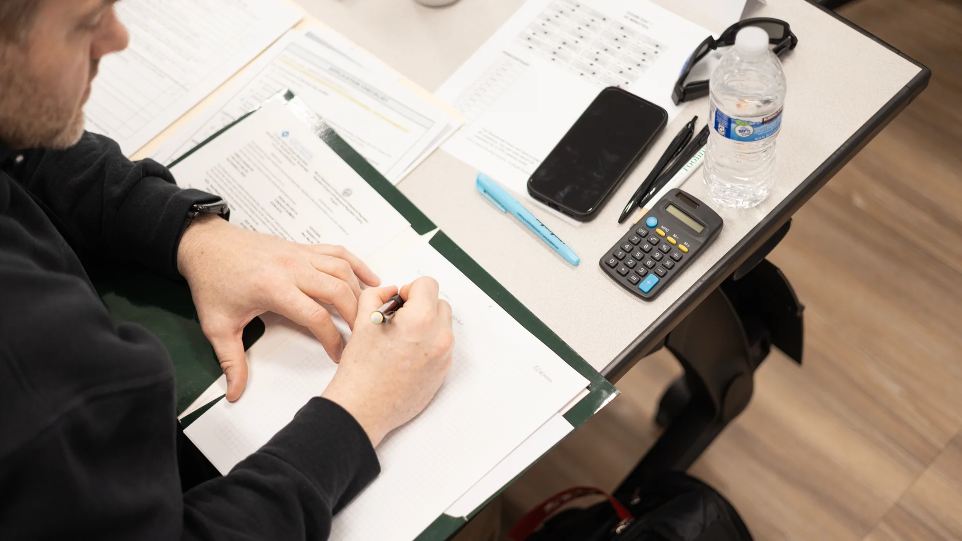 Student taking notes with a calculator and study materials during an Illinois Roofing Institute exam prep class