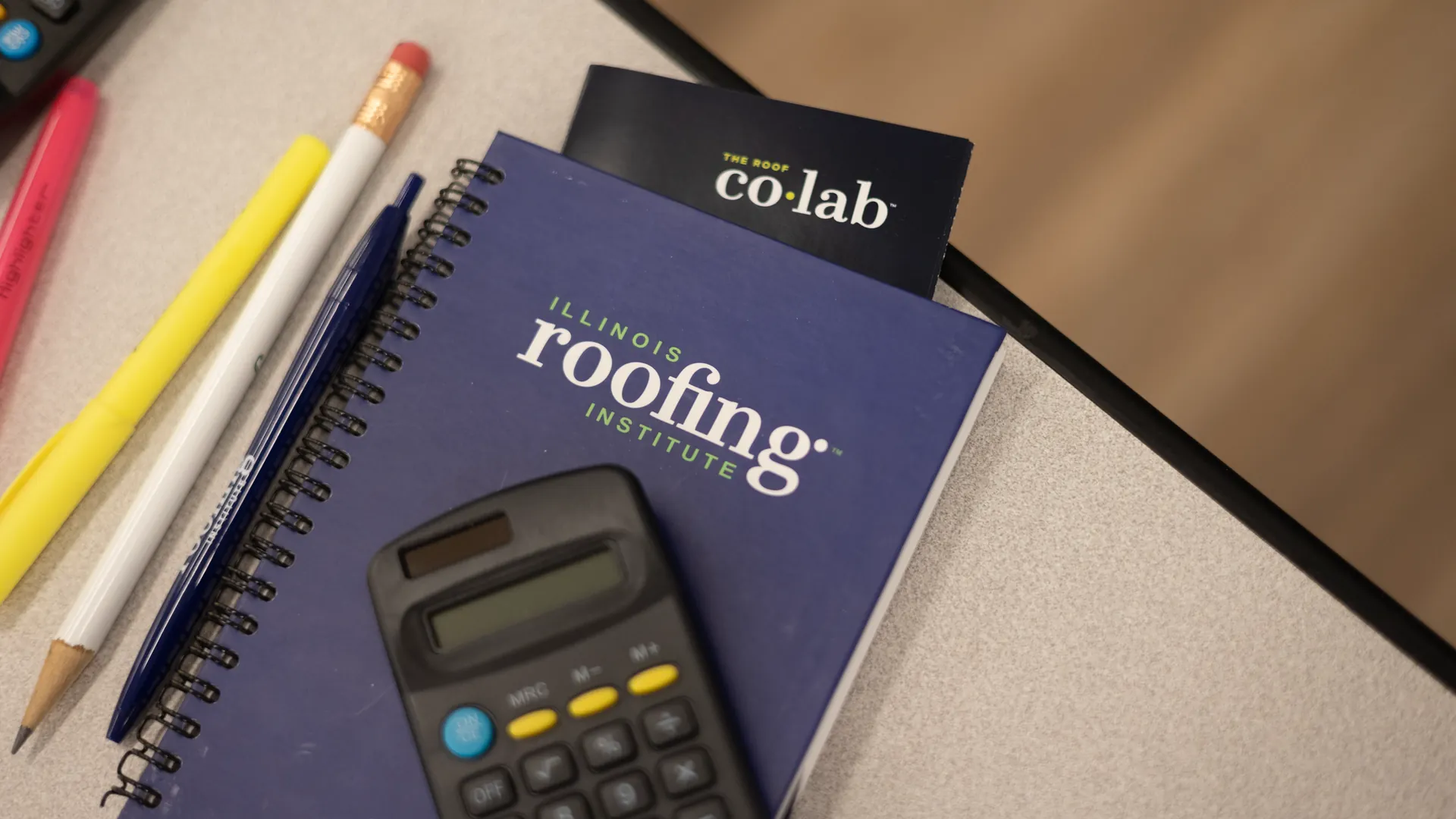 Materiales de la clase de roofing del Illinois Roofing Institute: cuaderno de estudio, calculadora y marcadores sobre la mesa